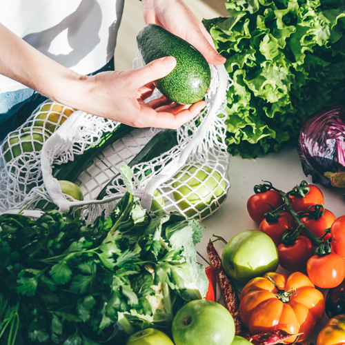 display of fresh fruit and vegetables being unpacked from a reusable grocery bag.