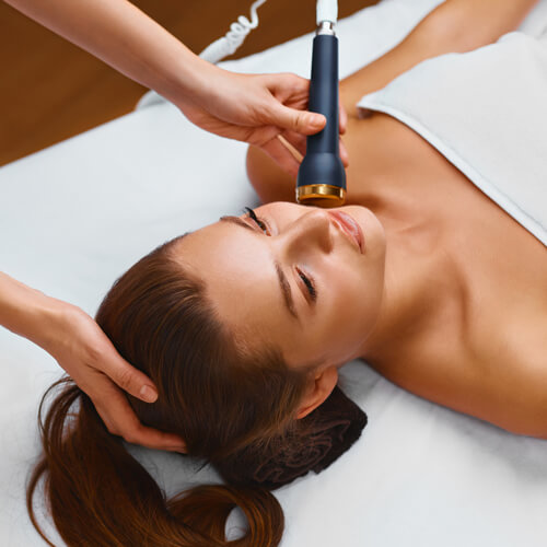 A woman lwith her eyes closed and lying on her back while receiving a microcurrent facial.