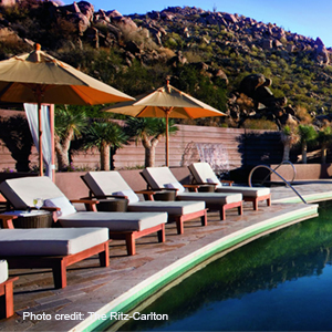 A row of lounge chairs frame one side of a pool at the Ritz Carlton