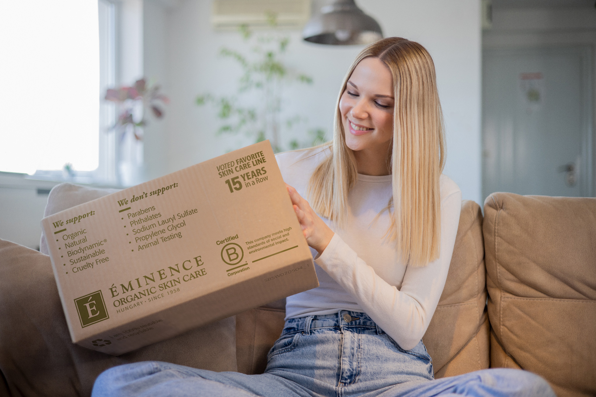 A woman holding an Eminence Organics box while sitting on a couch