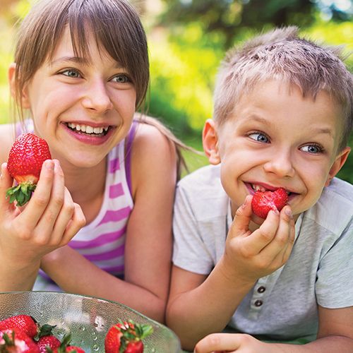 Two children eat strawberries outside