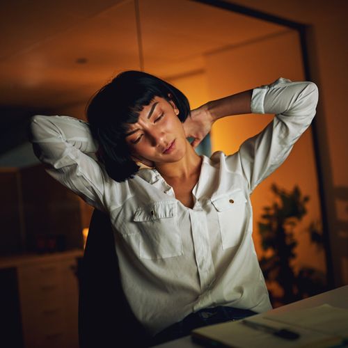 A woman stretches her neck to one side while bringing her hands to massage pain in the back of her neck