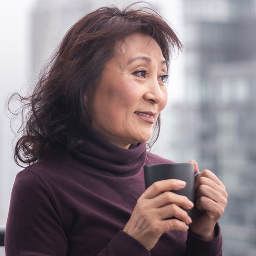 The side profile of a mature Asian woman holding a coffee mug.