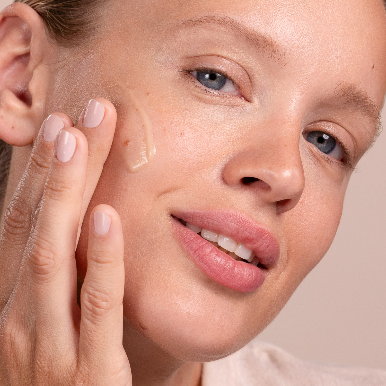 A woman applying the Eminence Organics Cornflower Recovery Serum to her face