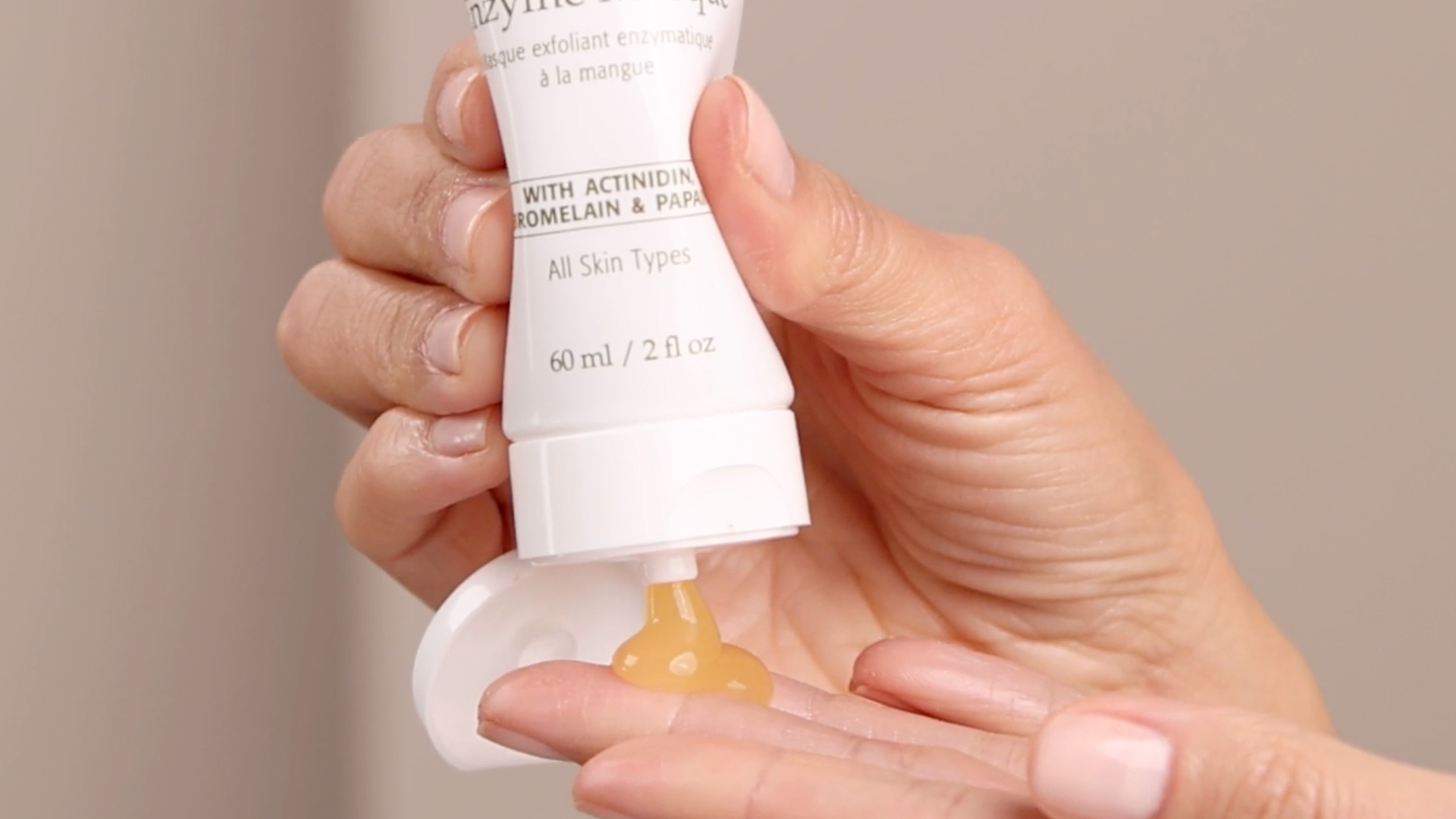 A person squeezing the Eminence Organics Mango Exfoliating Enzyme Masque tube onto the back of their hand