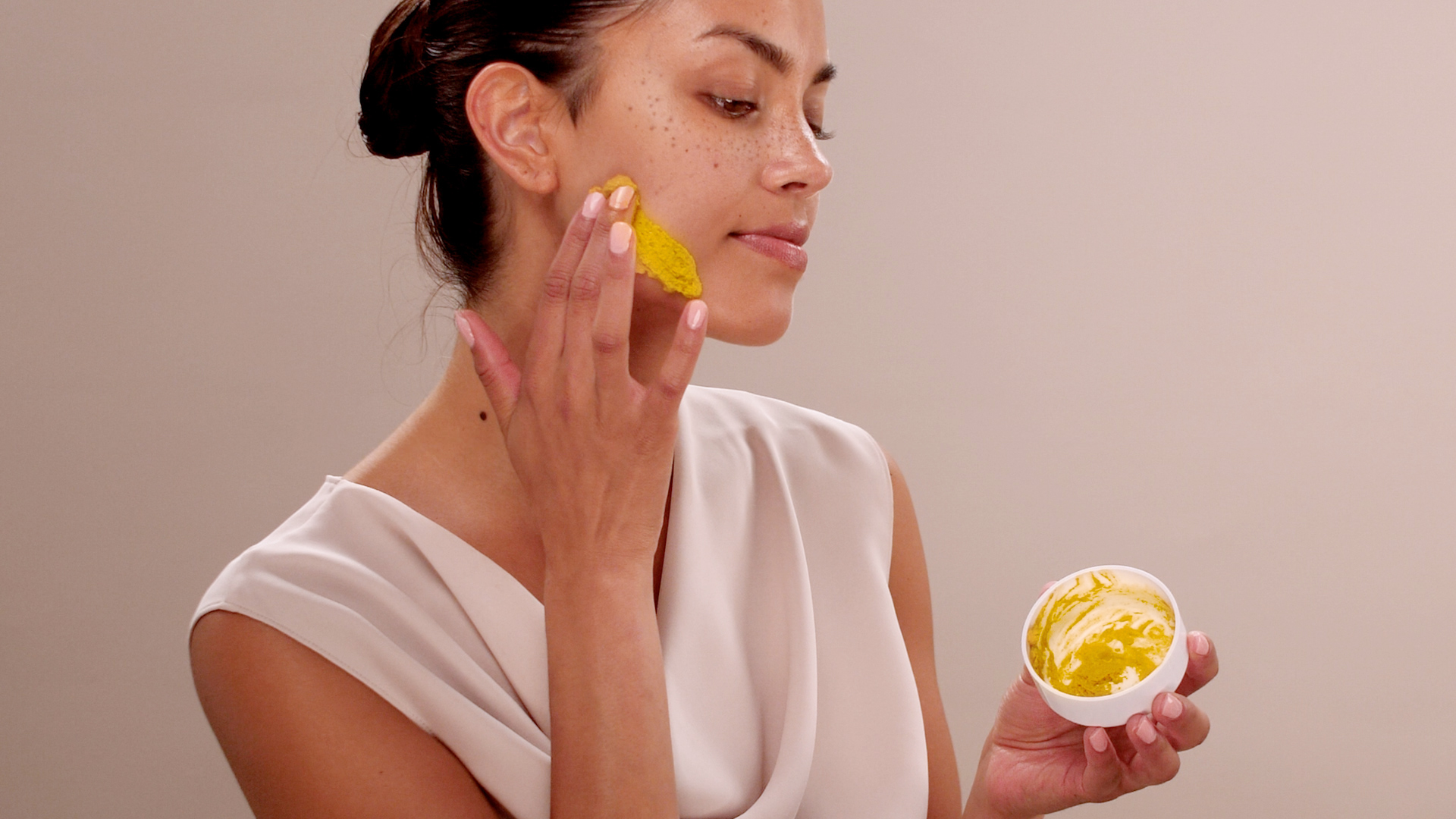 A woman with a swatch of the Eminence Organics Turmeric Energizing Treatment on her face