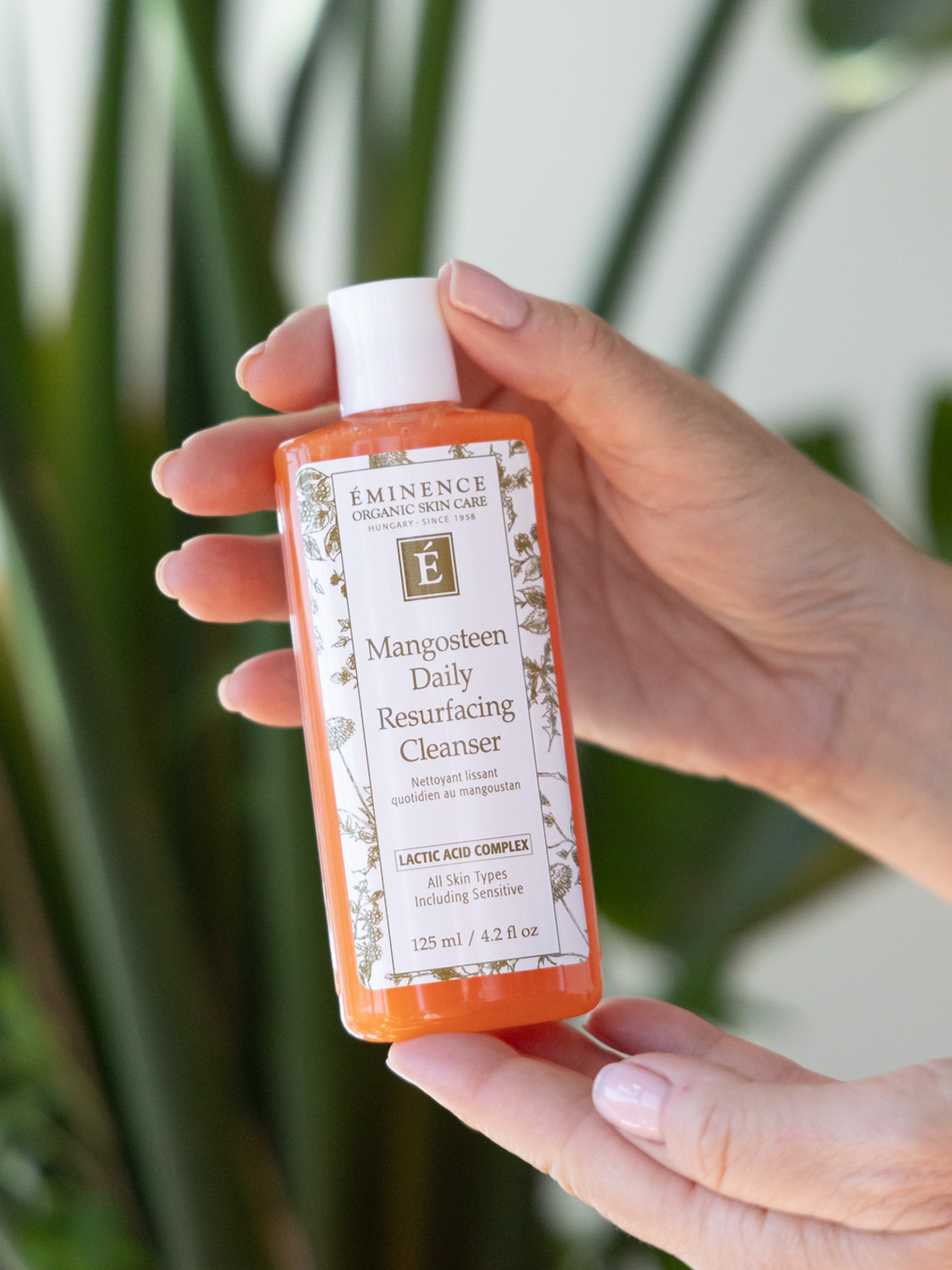 Two hands holding the Eminence Organics Mangosteen Daily Resurfacing Cleanser bottle