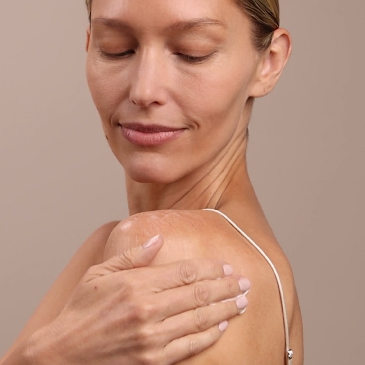 A woman applying the Eminence Organics Monoi Age Corrective Night Body Cream on her shoulder