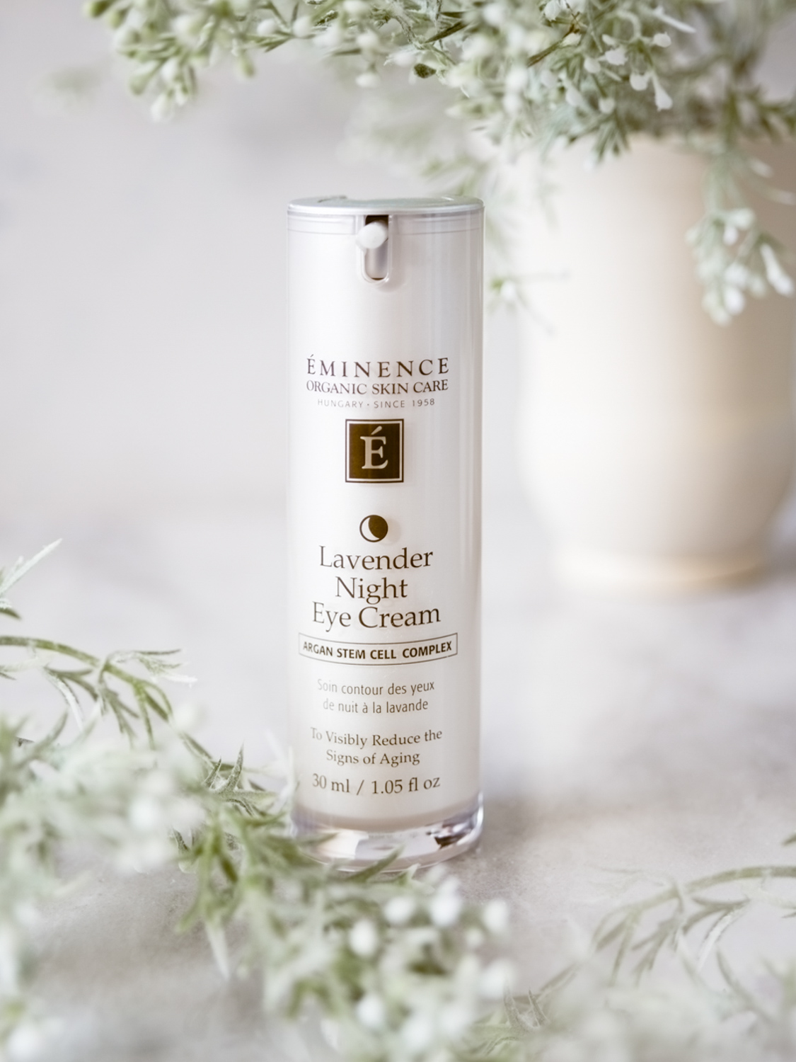 The Eminence Organics Lavender Night Eye Cream bottle surrounded by small white flowers