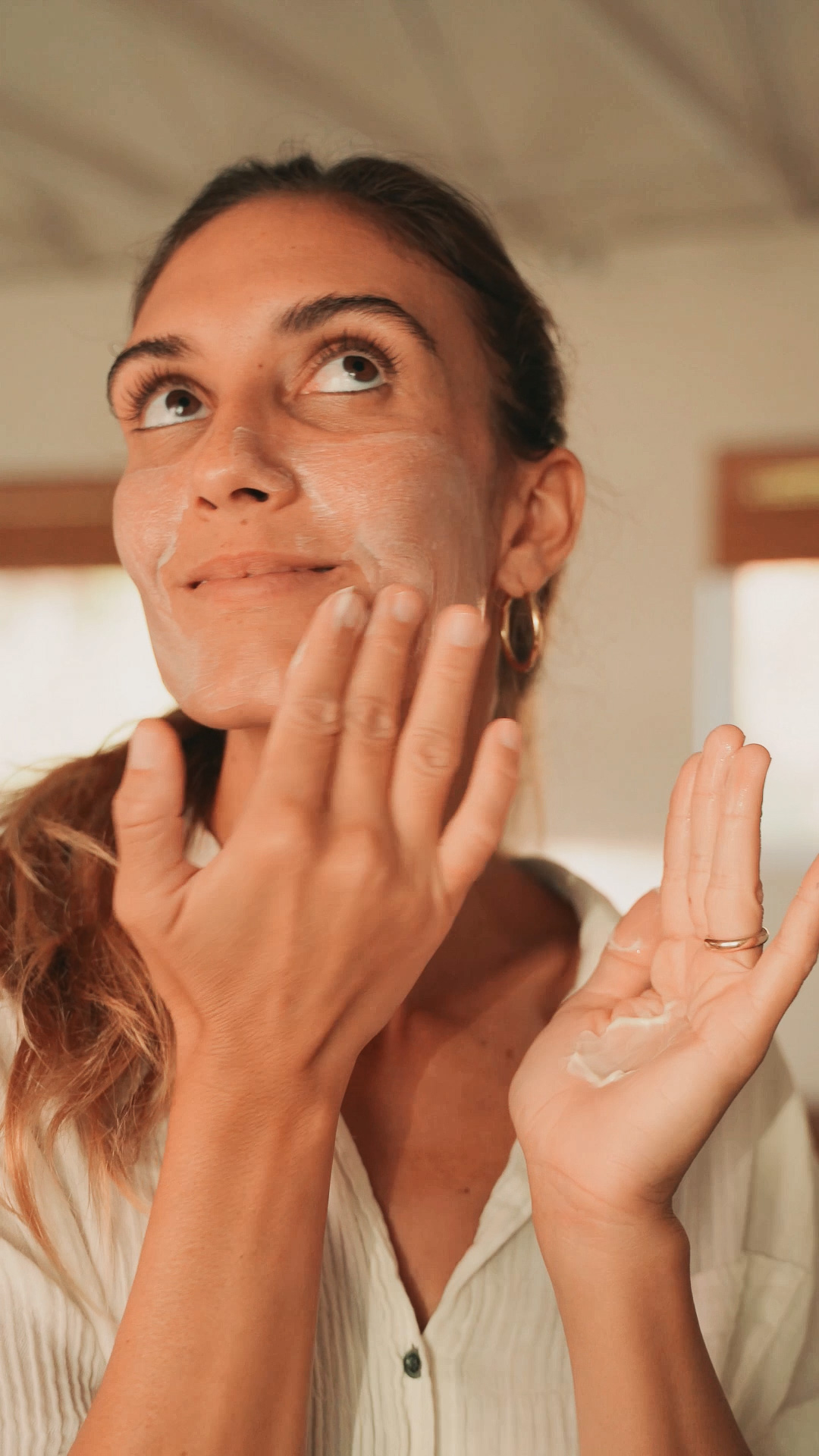A woman applying the Eminence Organics Monoi Age Corrective Exfoliating Cleanser onto her face