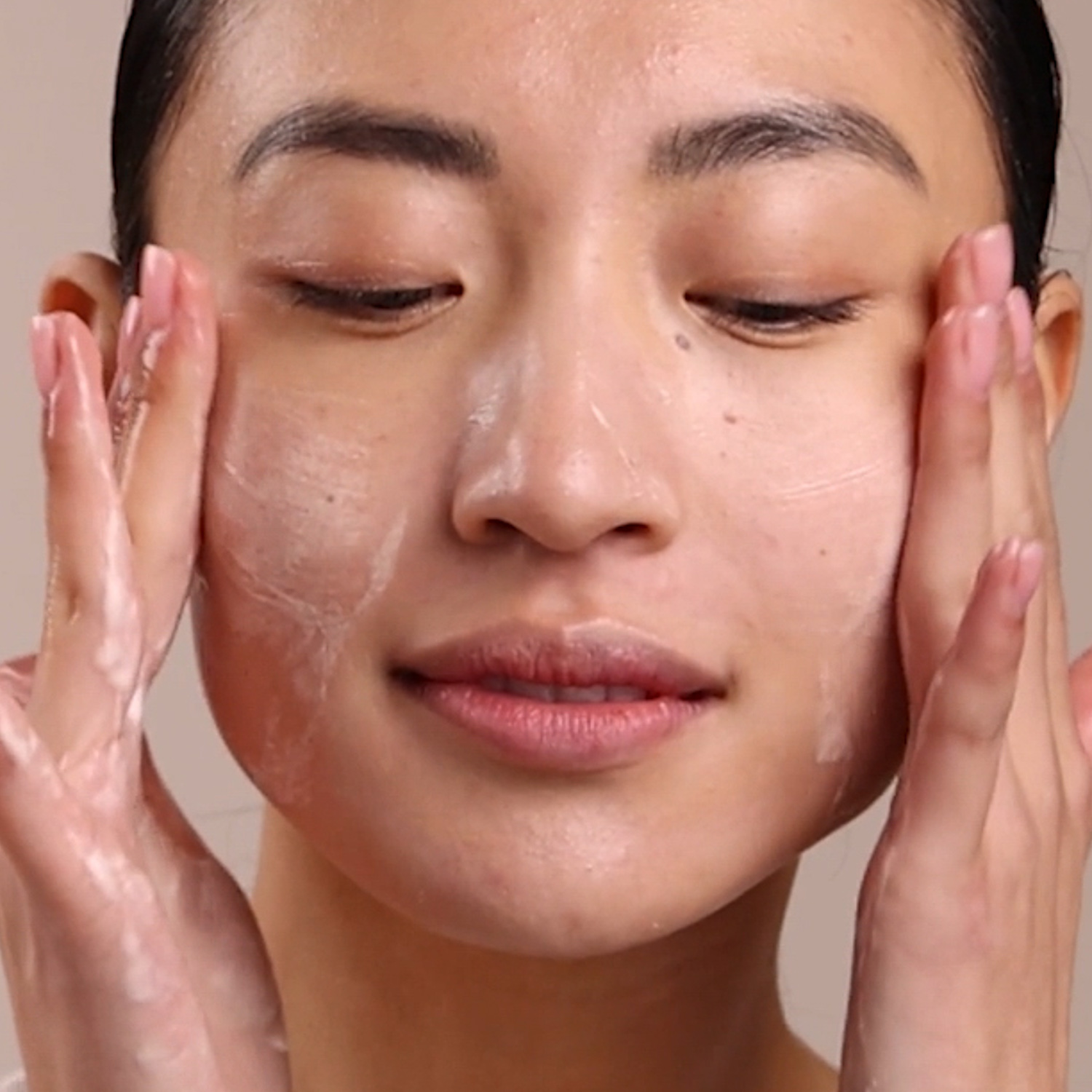A woman washing her face with the Eminence Organics Mangosteen Daily Resurfacing Cleanser