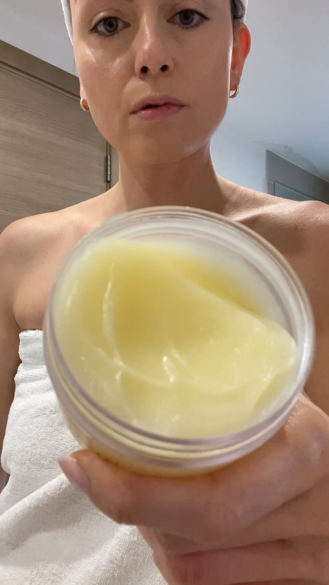 A woman holding an open jar of the Eminence Organics Yuzu Solid Body Oil