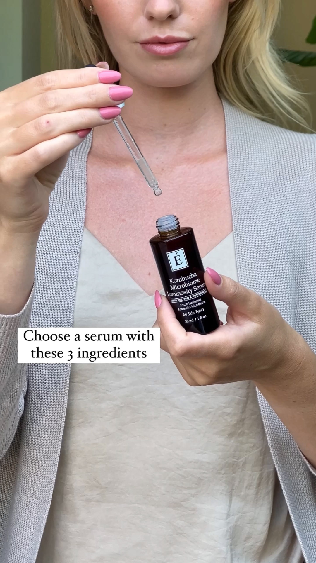 A woman holding the Eminence Organics Kombucha Microbiome Luminosity Serum dropper with one hand and the serum bottle with the other hand