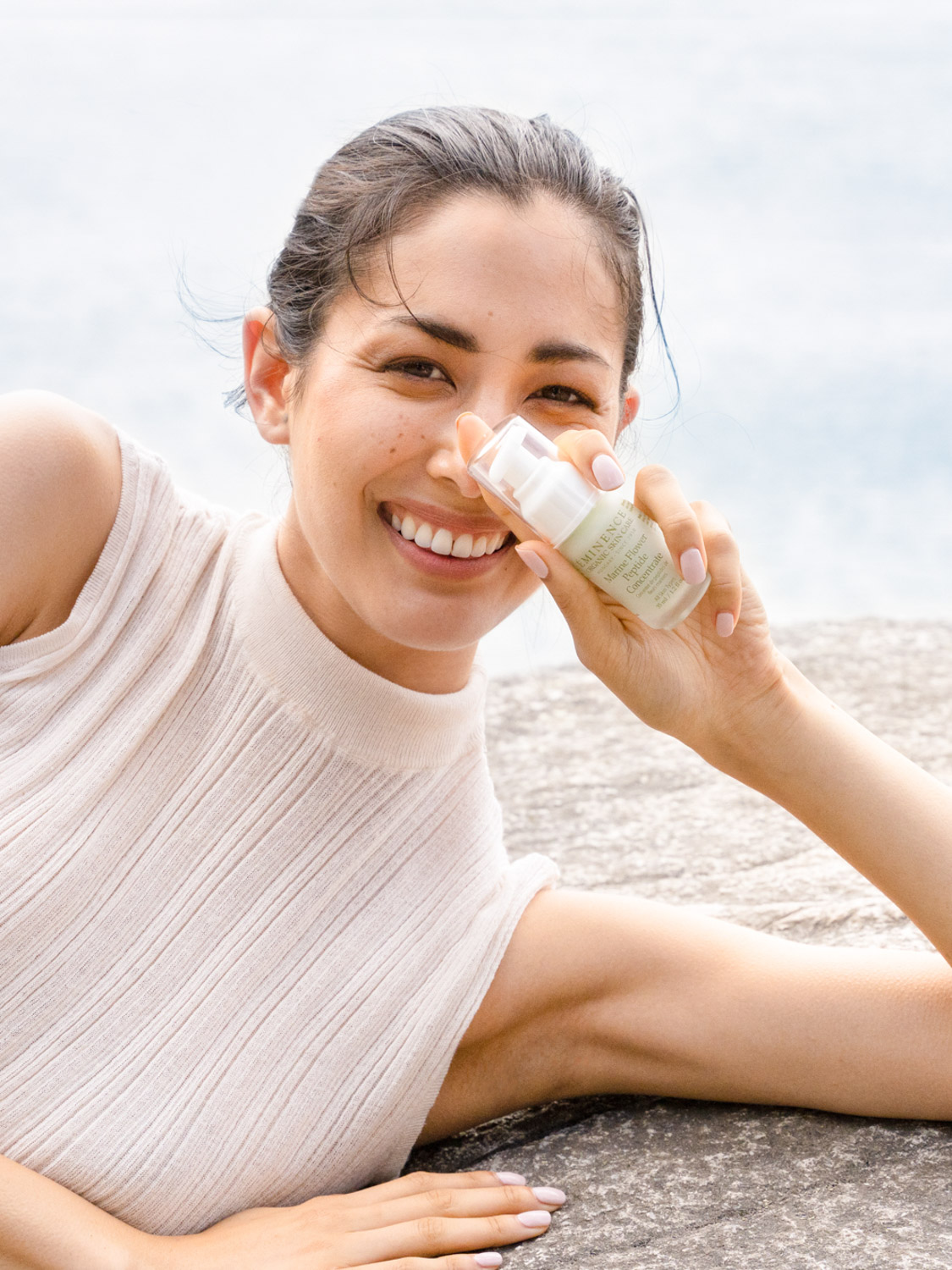 A woman holding the A hand holding the Eminence Organics Marine Flower Peptide Concentrate glass bottle