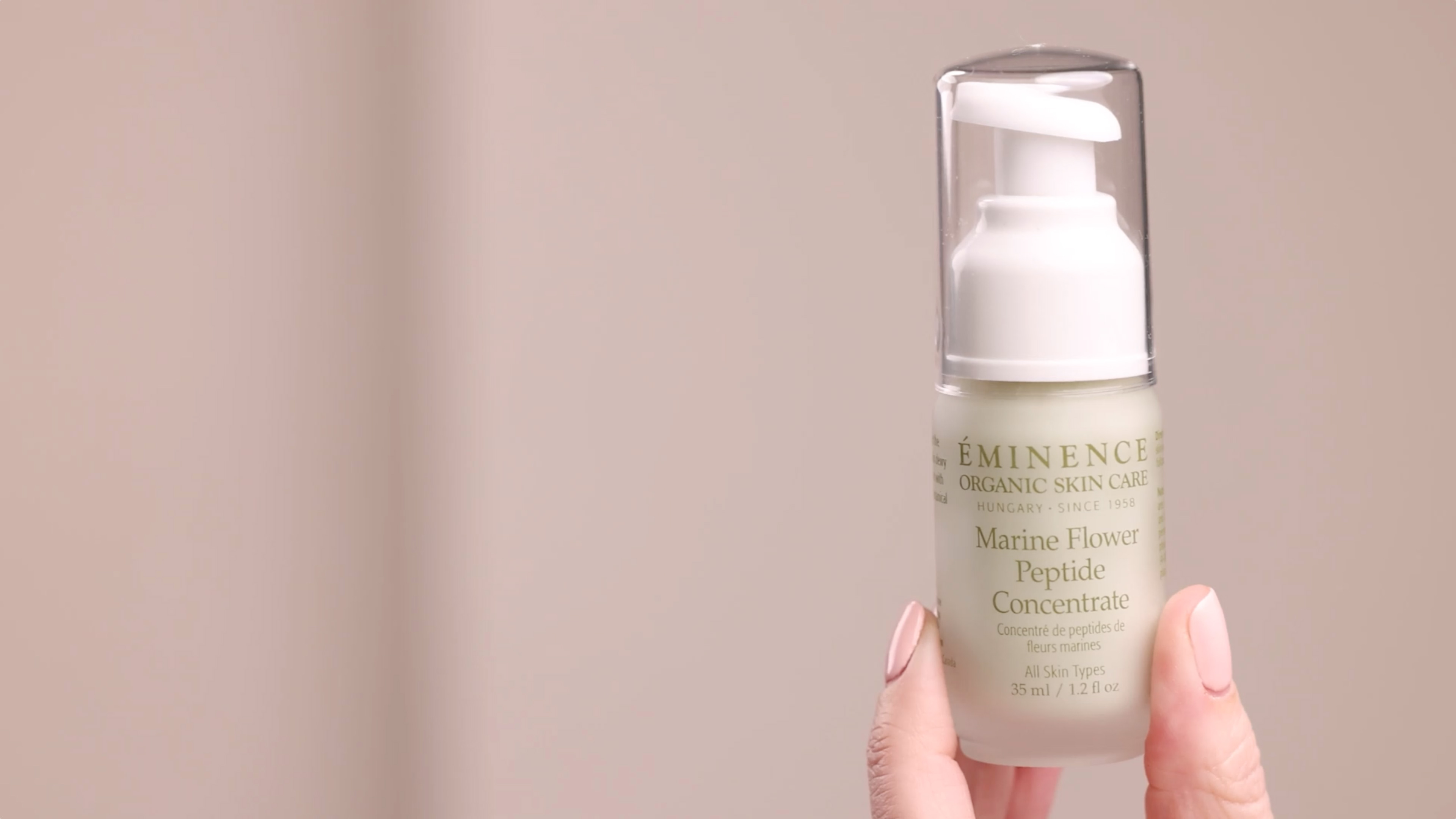 A hand holding the Eminence Organics Marine Flower Peptide Concentrate glass bottle