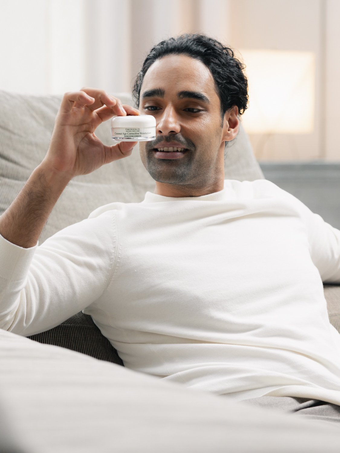 Relaxed man holding up Eminence Organics Coconut Age Corrective Moisturizer in front of face