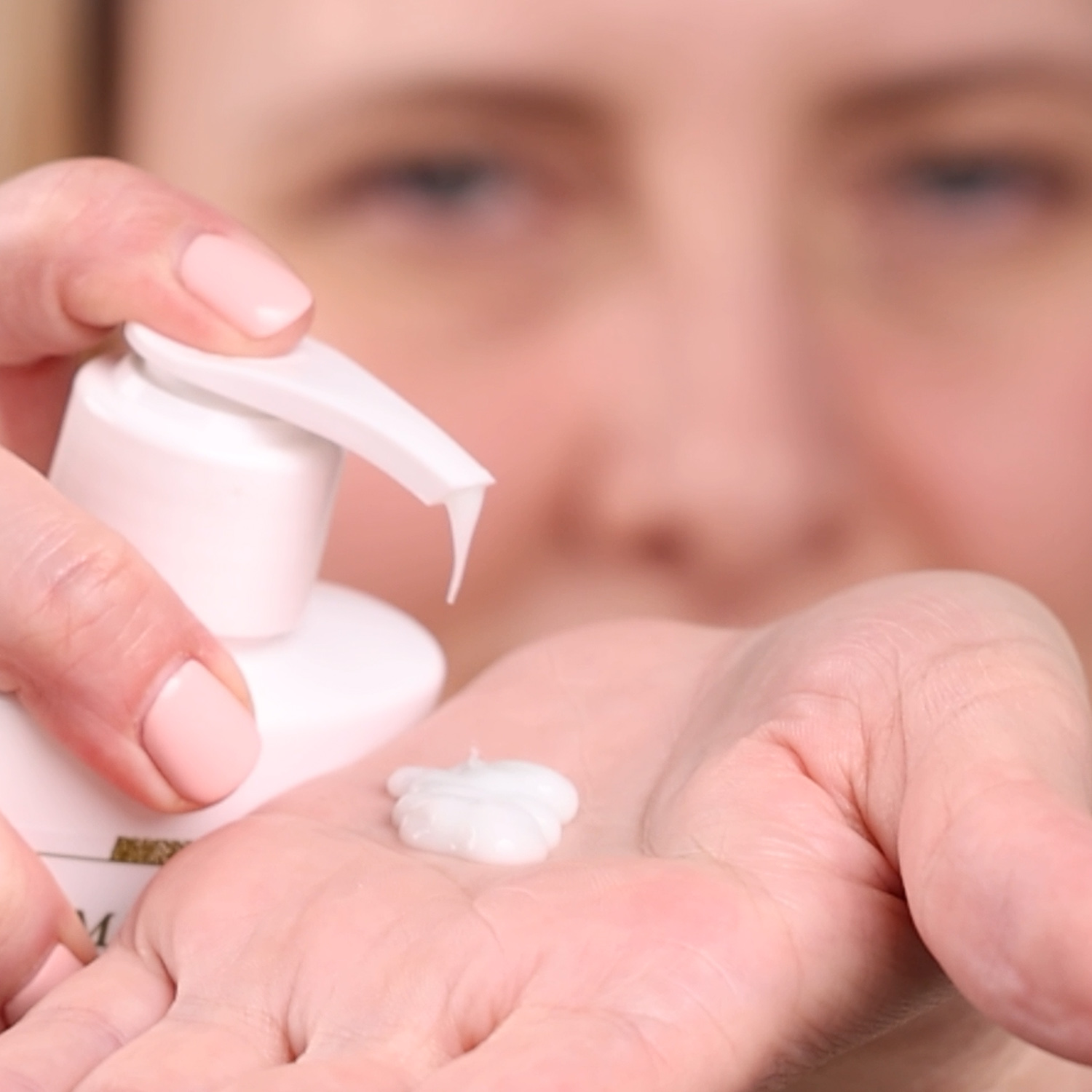 A hand holding a small amount of Eminence Organics Stone Crop Body Lotion dispensed from a pump bottle