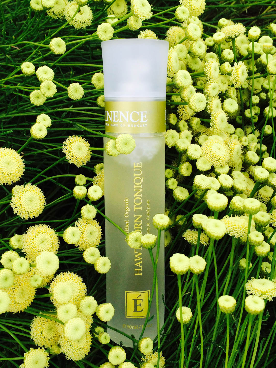The Eminence Organics Hawthorn Tonique glass bottle surrounded by yellow flowers