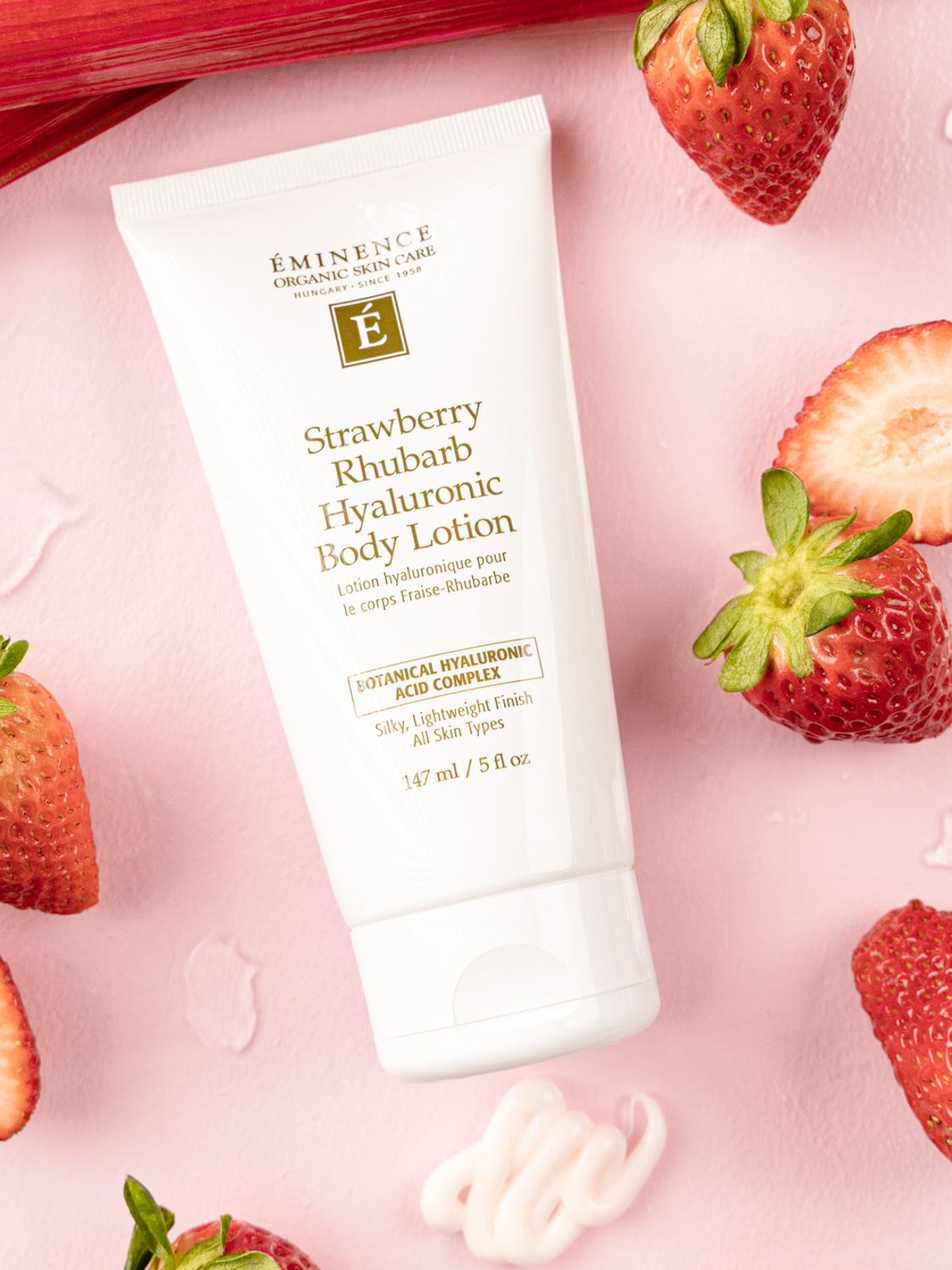 Eminence Organics Strawberry Rhubarb Hyaluronic Body Lotion on a pink background surrounded by strawberries