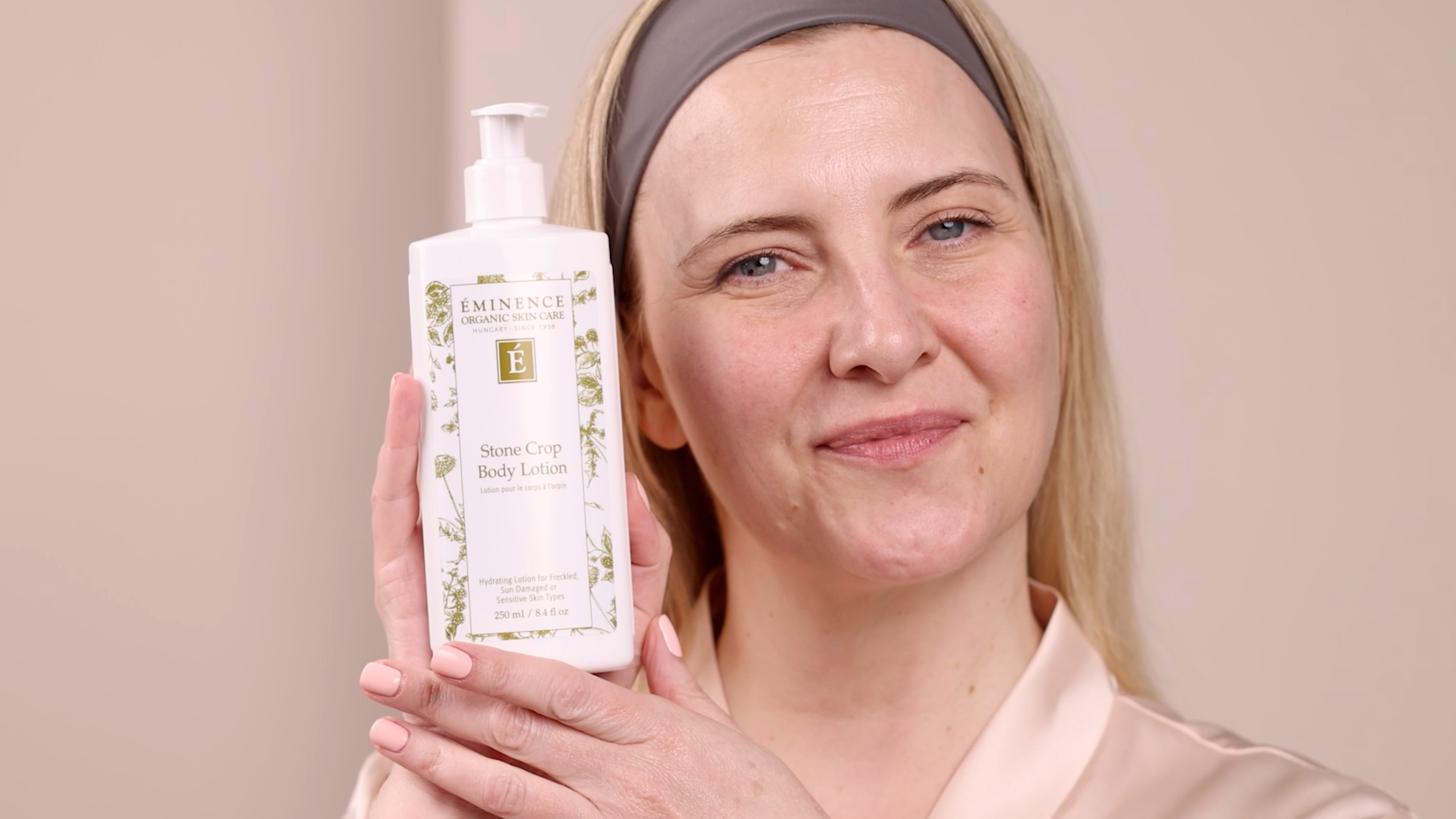 A woman holding the Eminence Organics Stone Crop Body Lotion next to her
