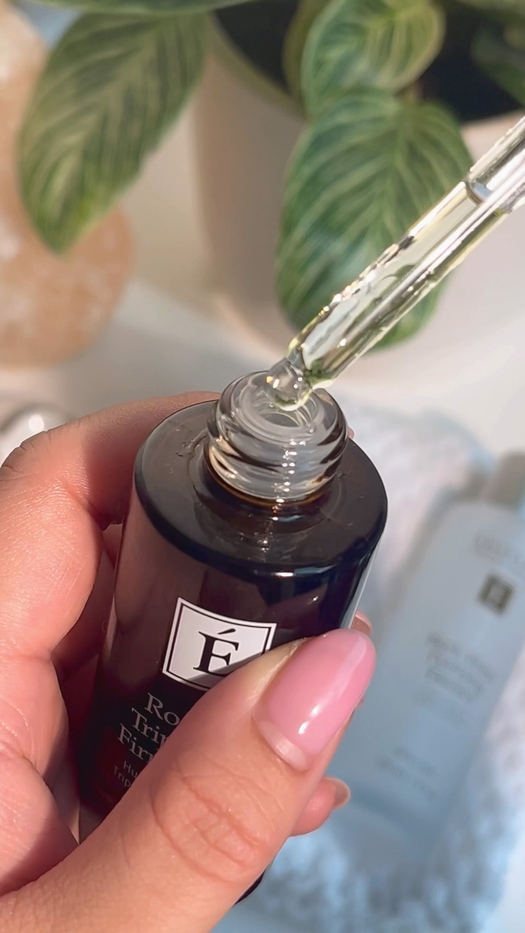 A hand holding the Eminence Organics Rosehip Triple C+E Firming Oil with the dropper filled with the oil