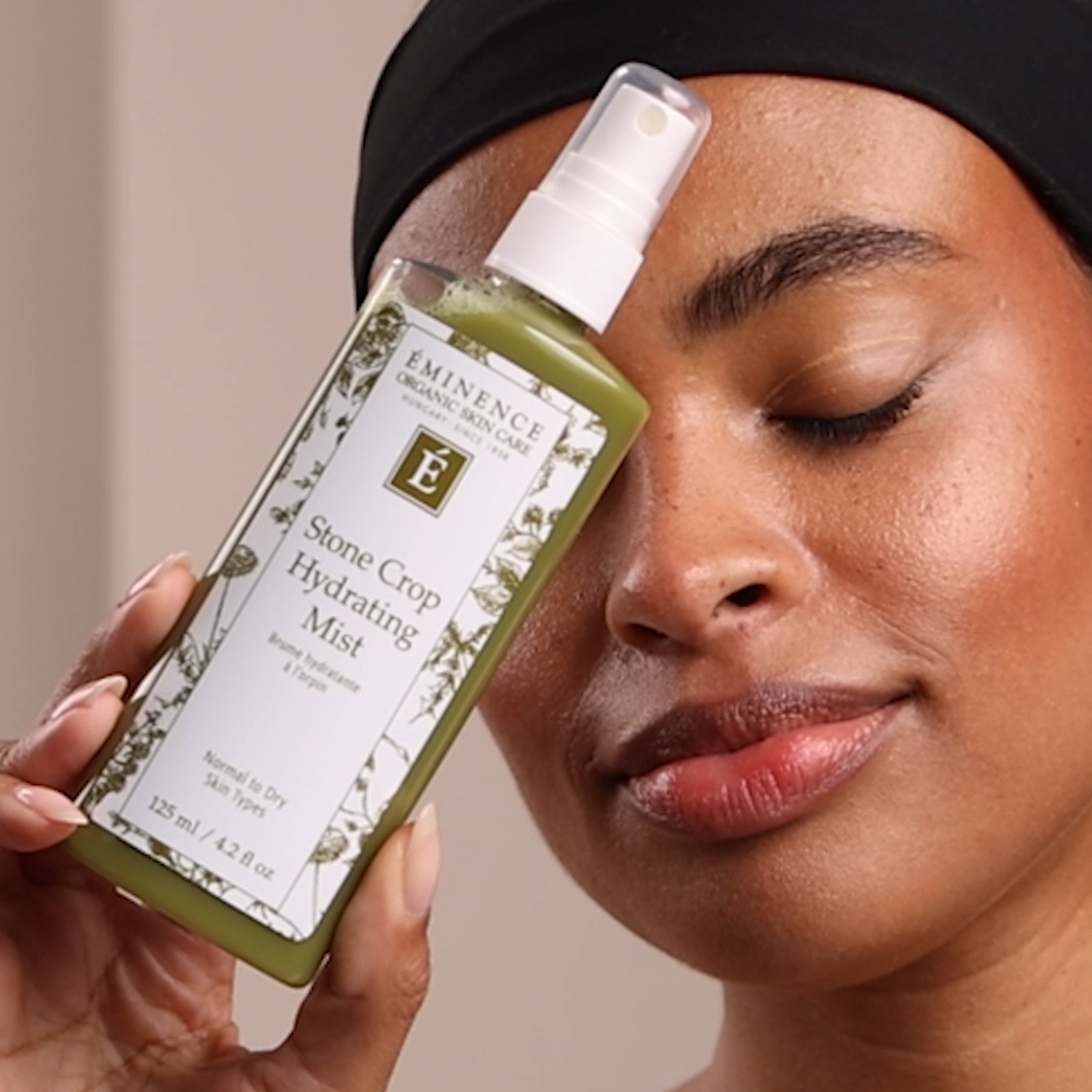 A woman holding the Eminence Organics Stone Crop Hydrating Mist next to her face