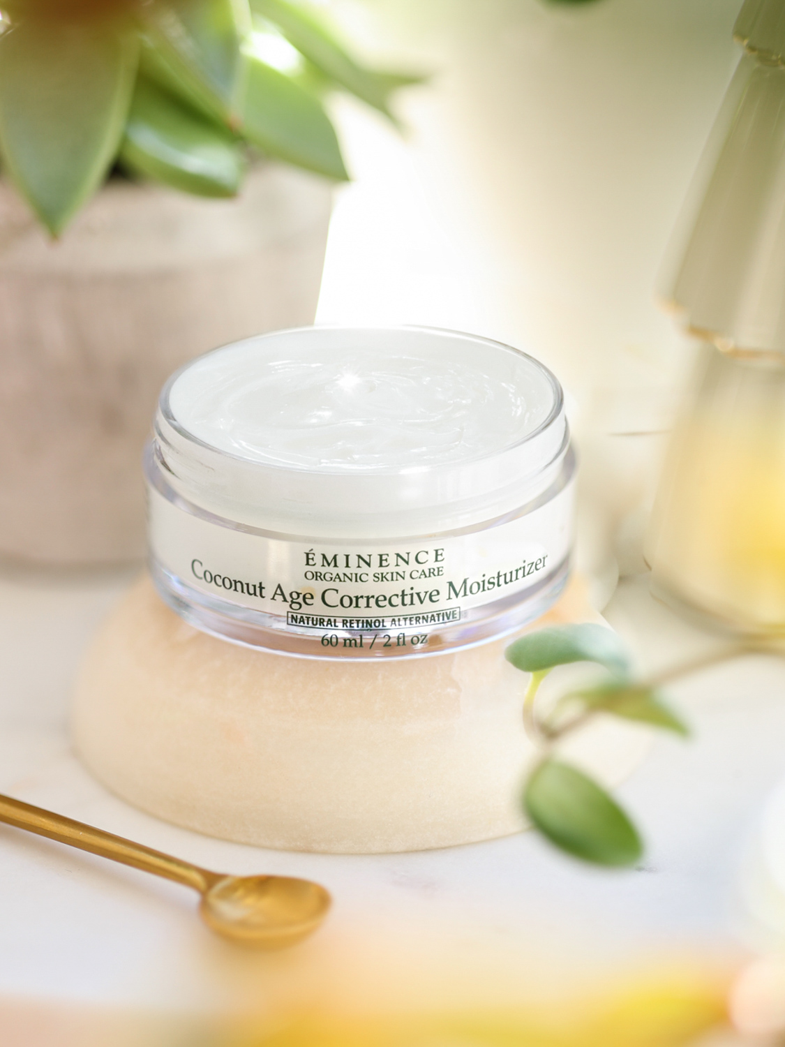 Open jar of Eminence Organics Coconut Age Corrective Moisturizer with a golden spoon on the side