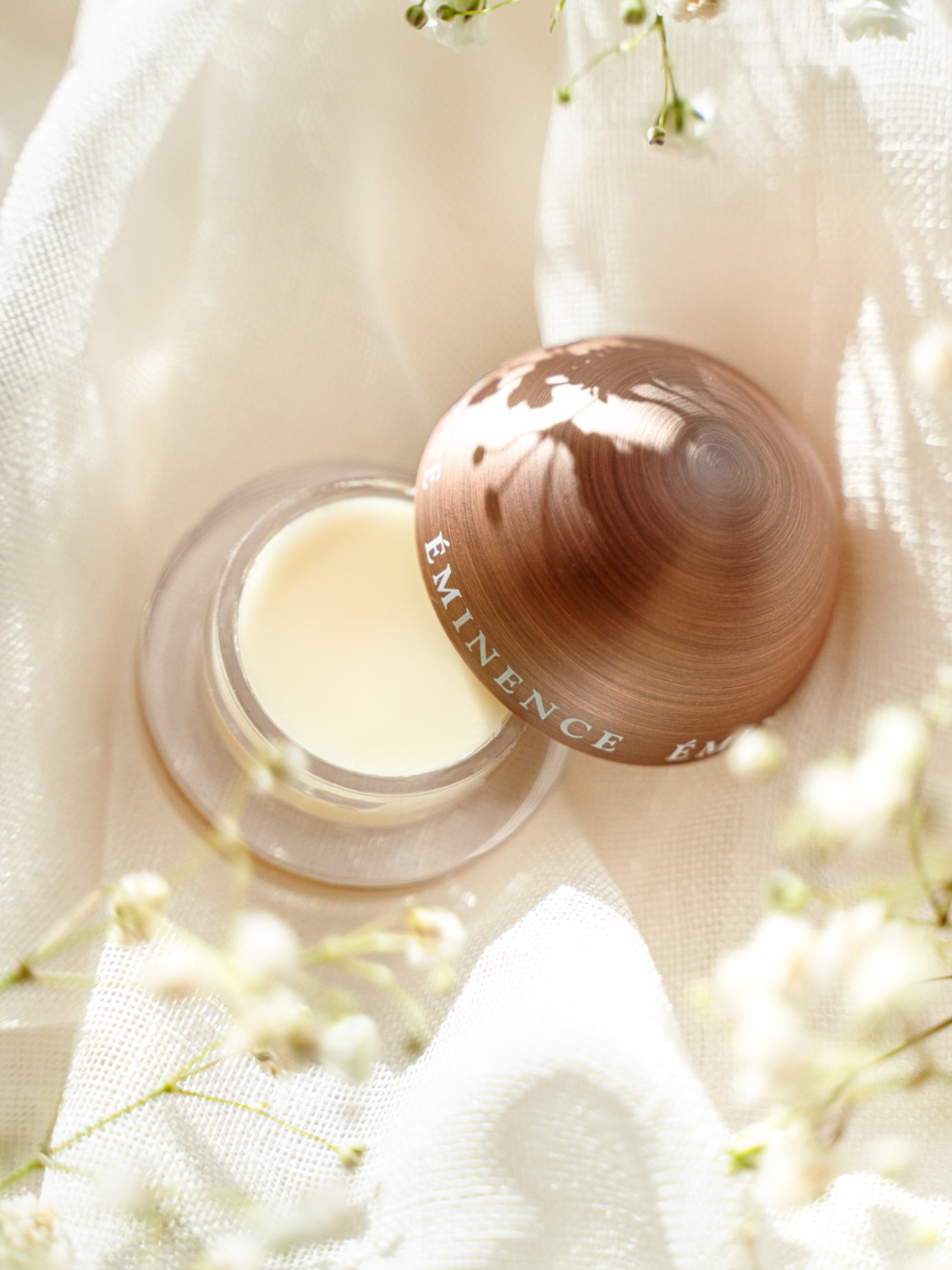 Eminence Organics Citrus Lip Balm with open lid on a white cloth backdrop