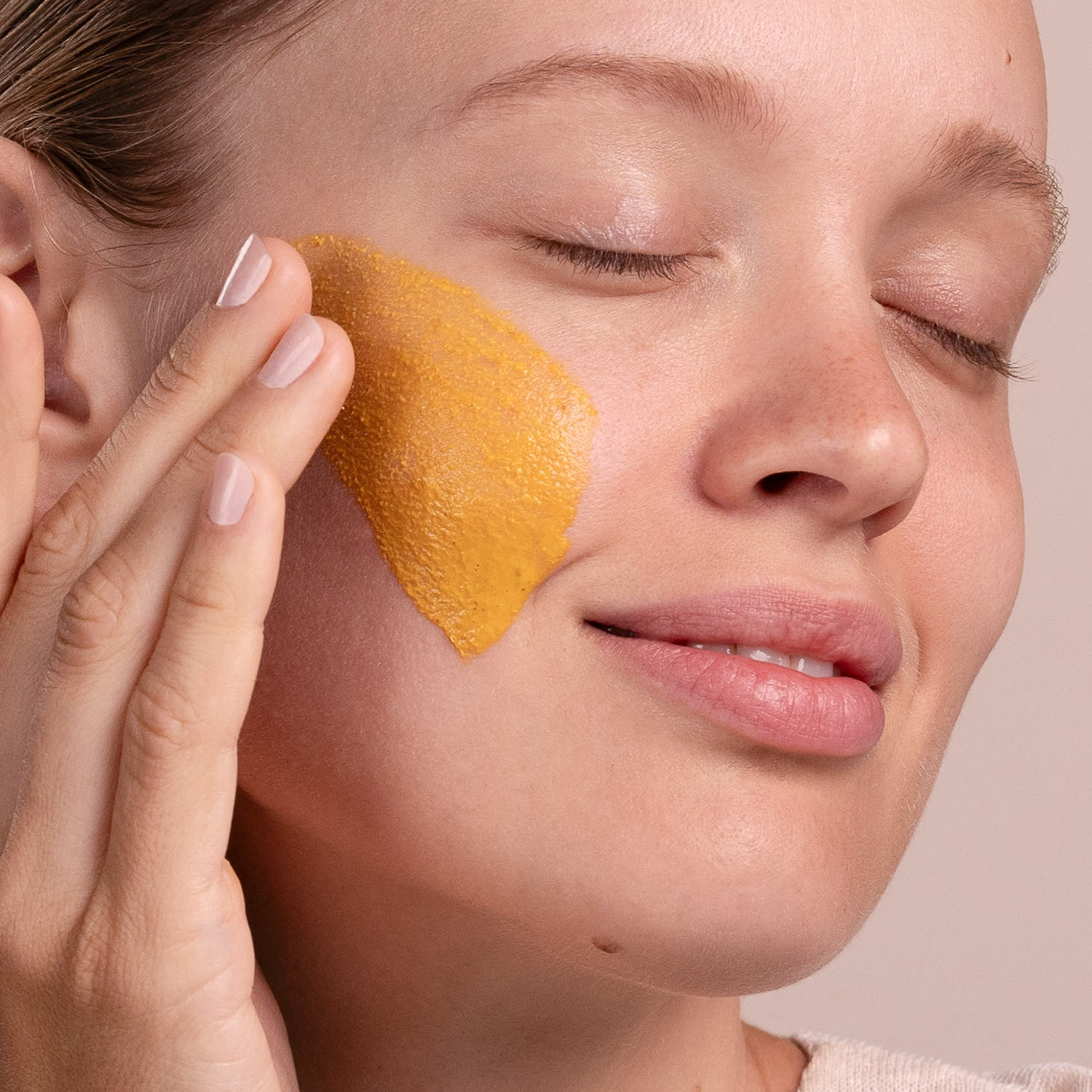 A woman with a swatch of the Eminence Organics Turmeric Energizing Treatment on her face