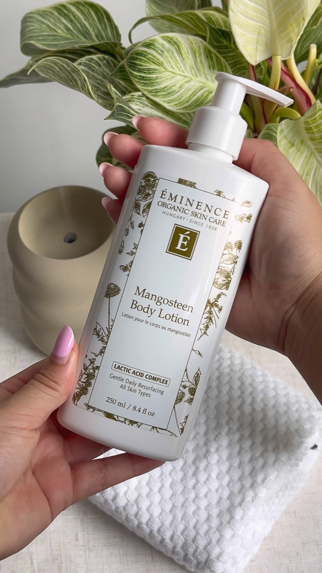 A person holding the Eminence Organics Mangosteen Body Lotion bottle