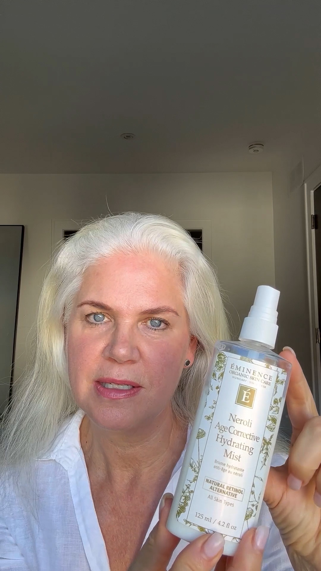 A woman holding the Eminence Organics Neroli Age Corrective Hydrating Mist Bottle