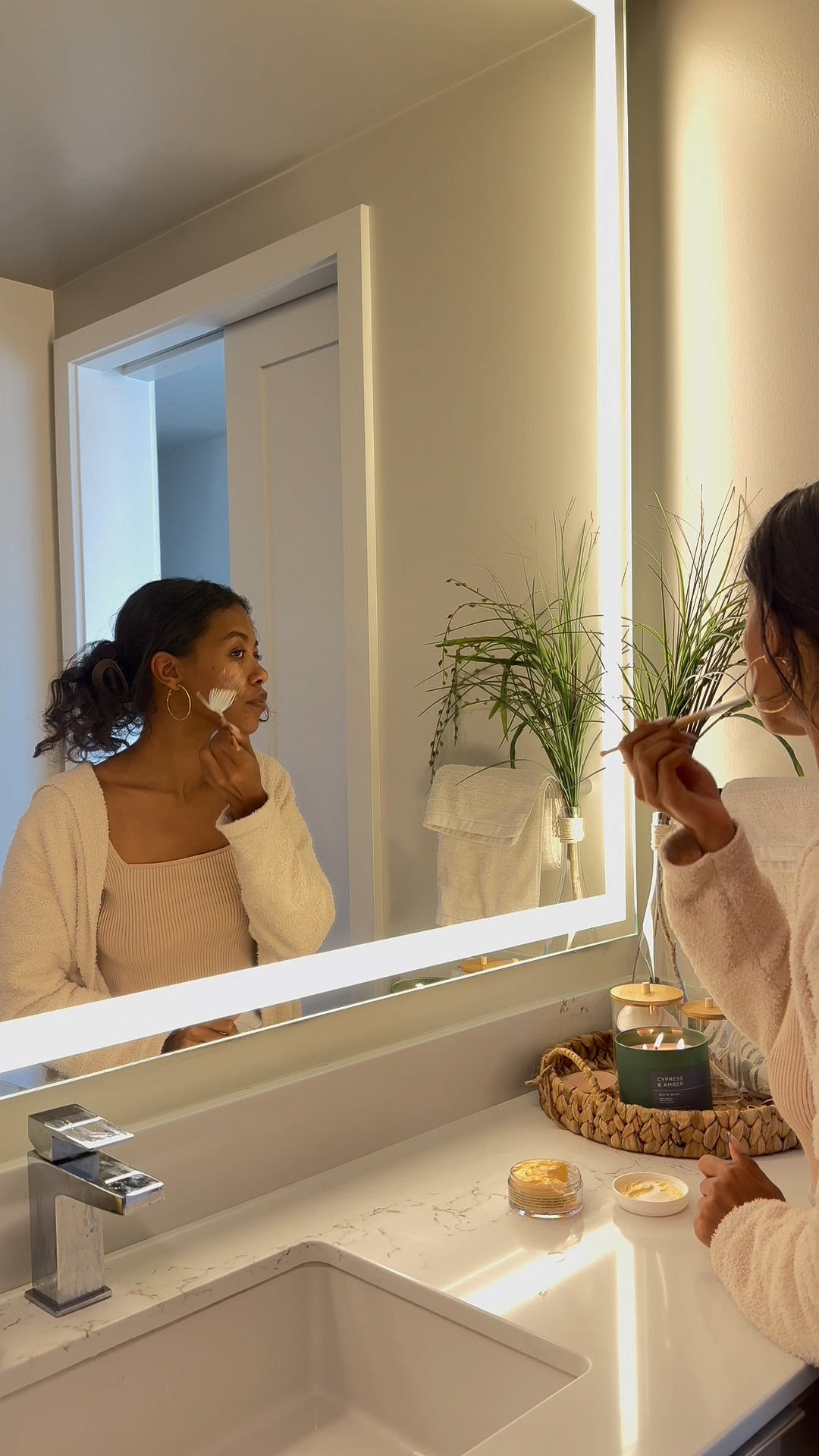 A person applying the Eminence Organics Linden Calendula Treatment to their face in front of a mirror