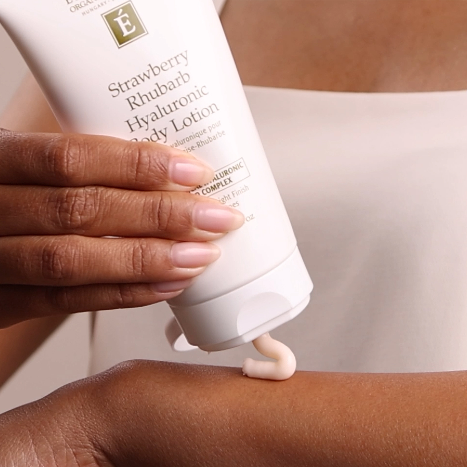A woman applying the Eminence Organics Strawberry Rhubarb Hyaluronic Body Lotion on her arm