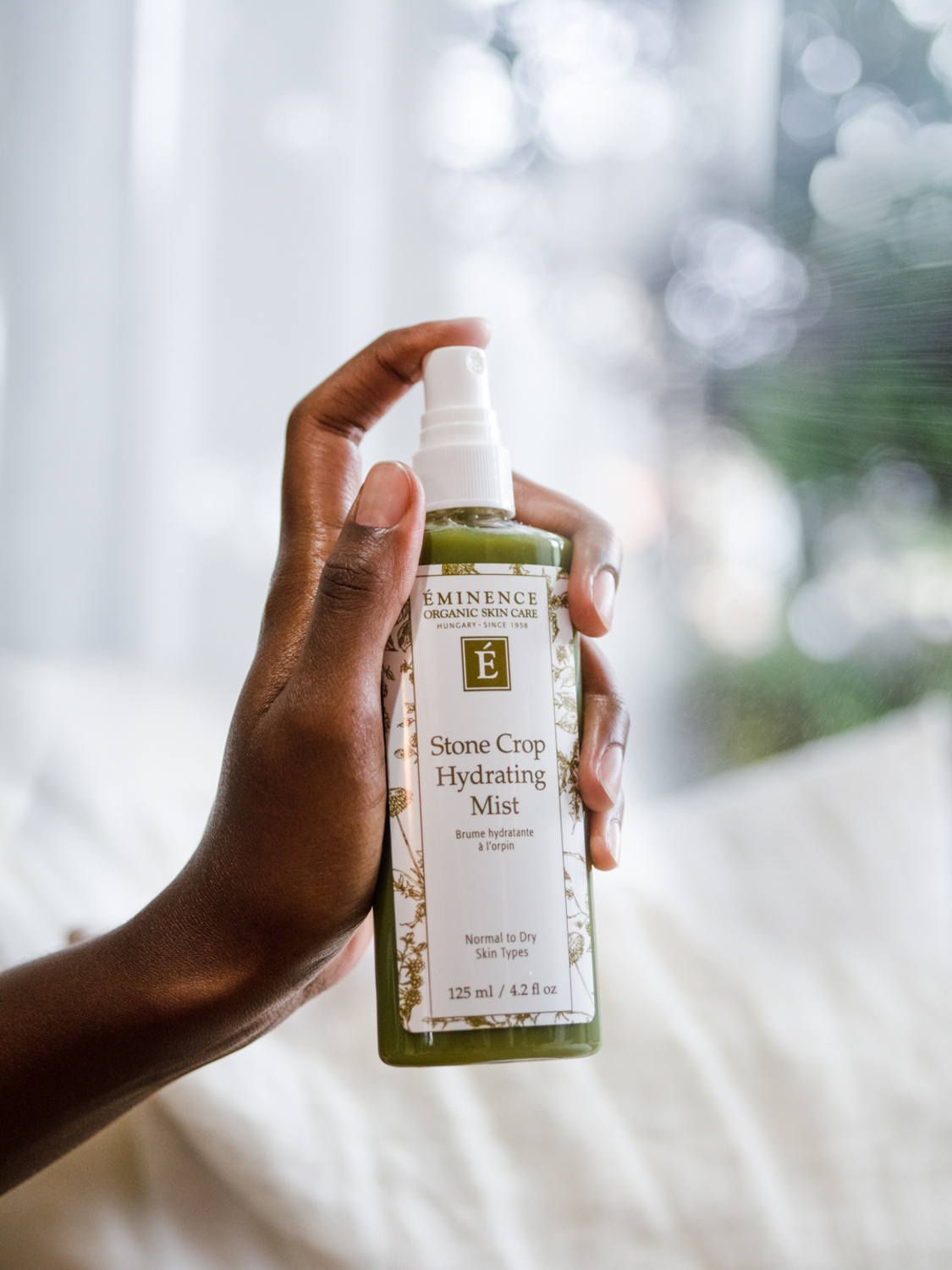A hand holding the Eminence Organics Stone Crop Hydrating Mist