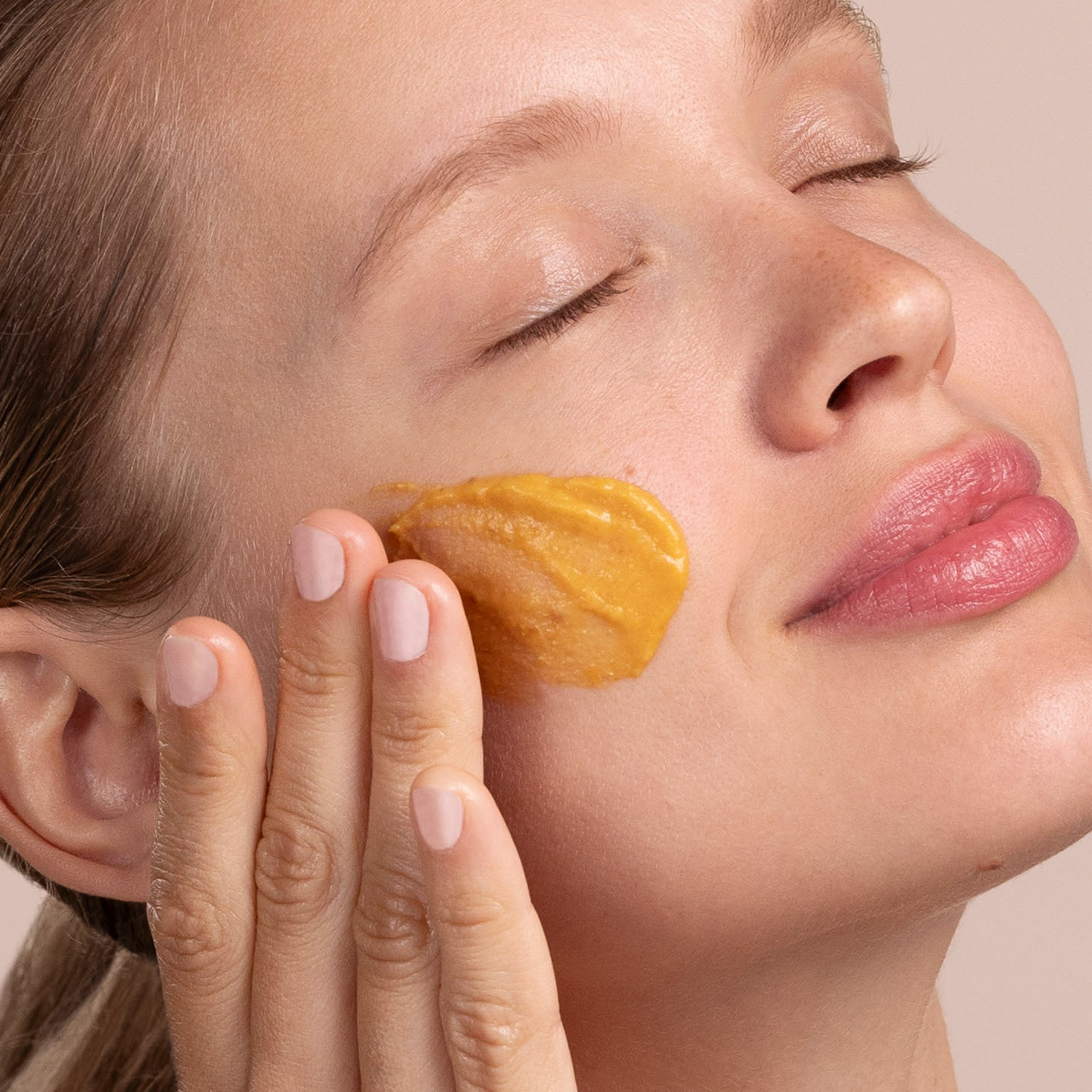 A woman with a swatch of the Eminence Organics Pumpkin Latte Hydration Masque on her face