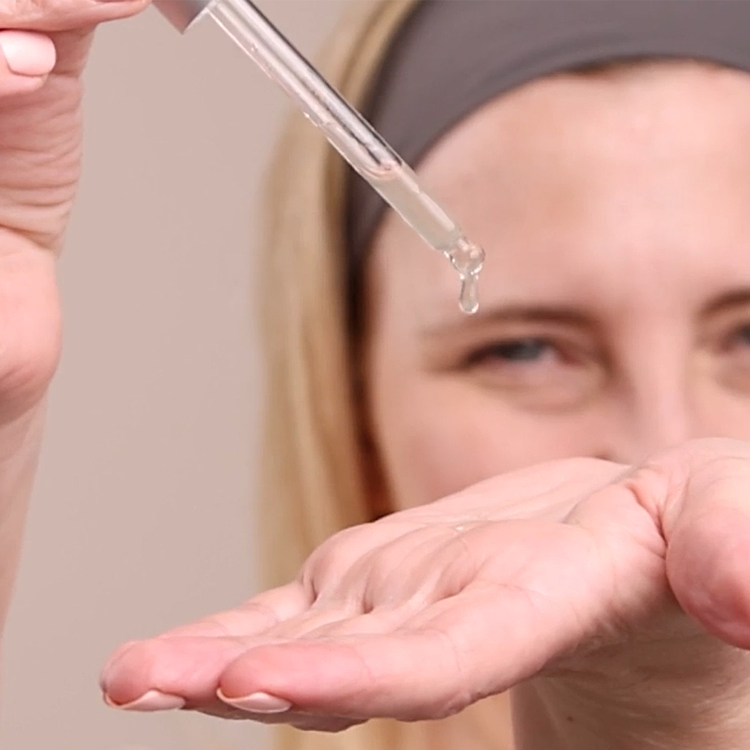 A close up to a woman holding the Eminence Organics Kombucha Microbiome Luminosity Serum dropper near her face