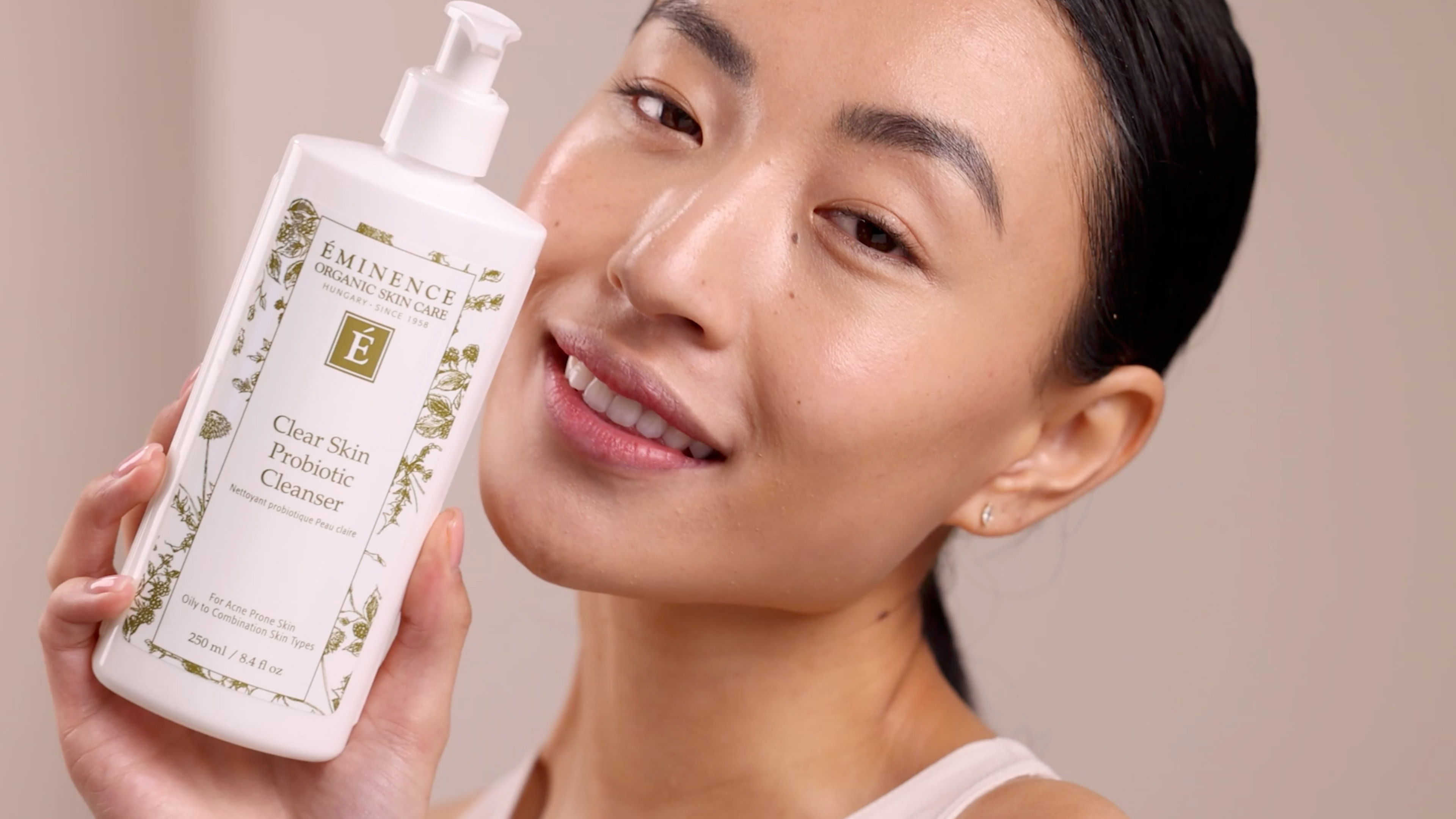 Happy woman holding Eminence Organics Clear Skin Probiotic Cleanser next to face