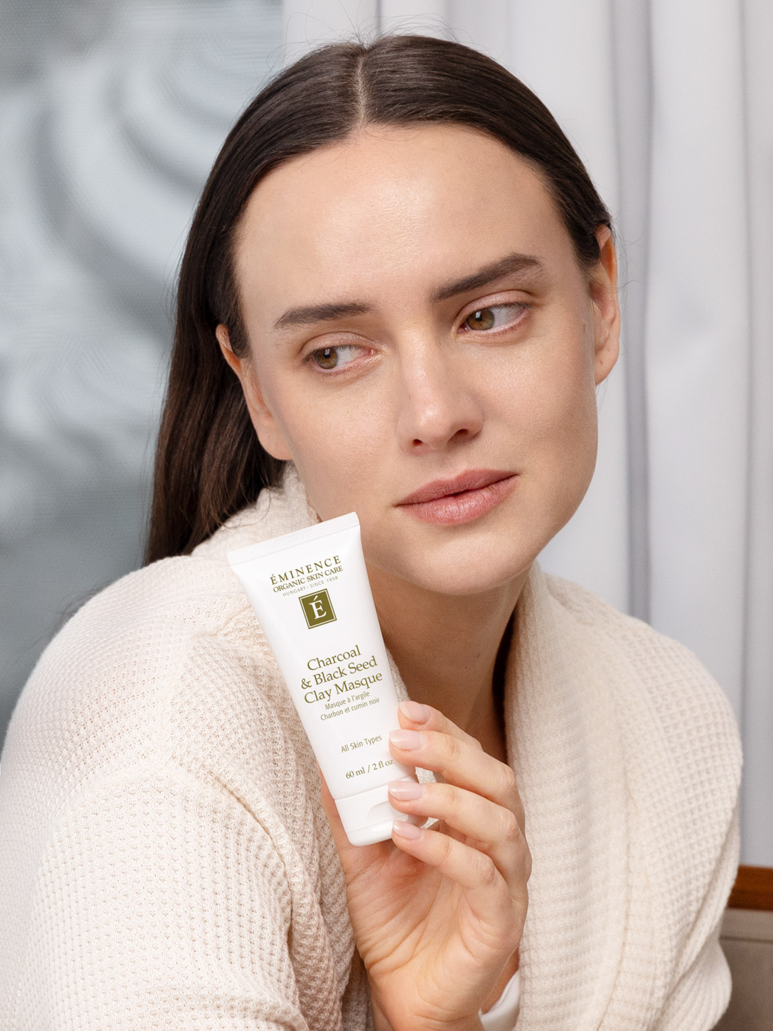 A woman holding Eminence Organics Charcoal & Black Seed Clay Masque
