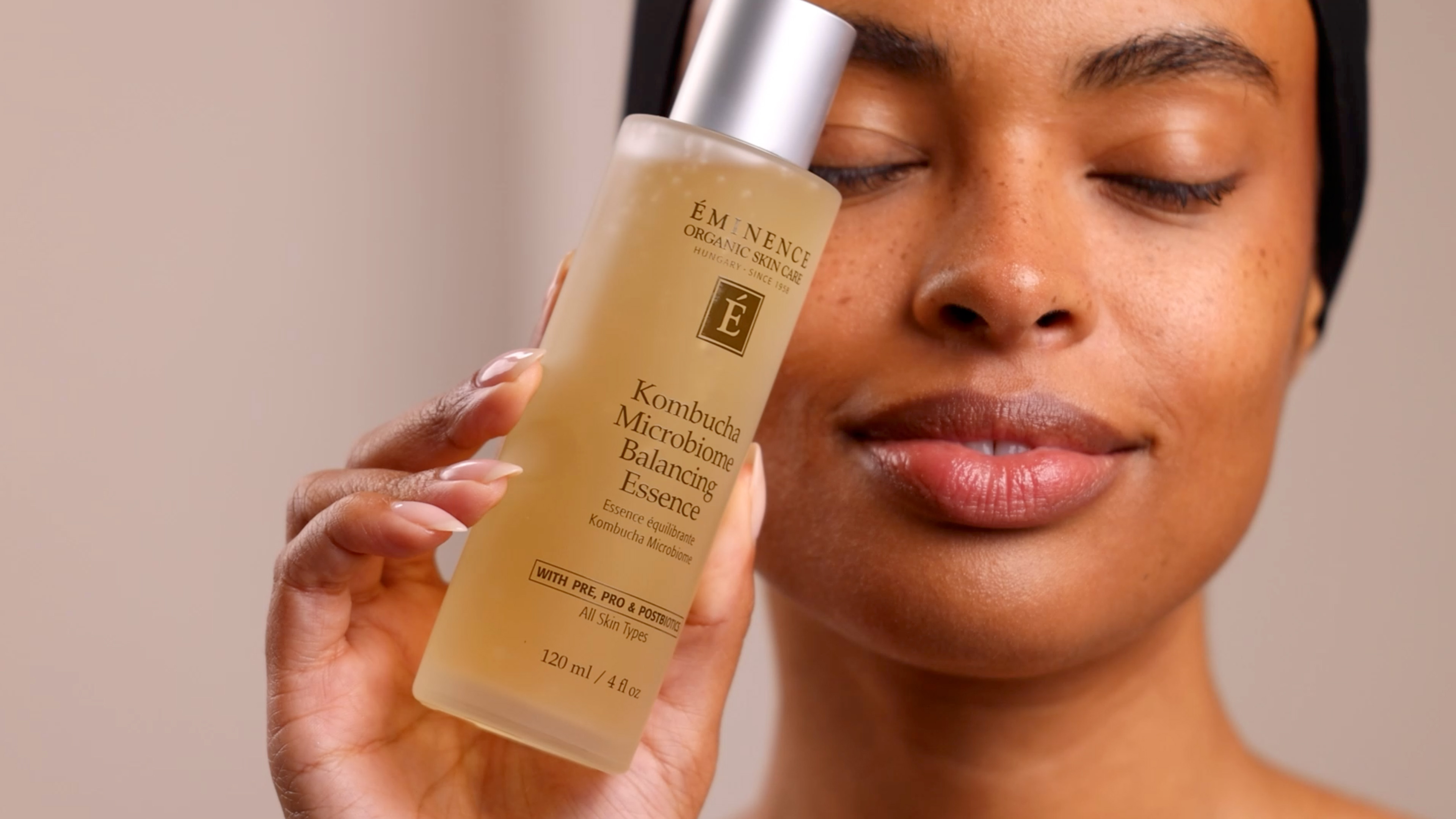 A woman holding the Eminence Organics Kombucha Microbiome Balancing Essence glass bottle