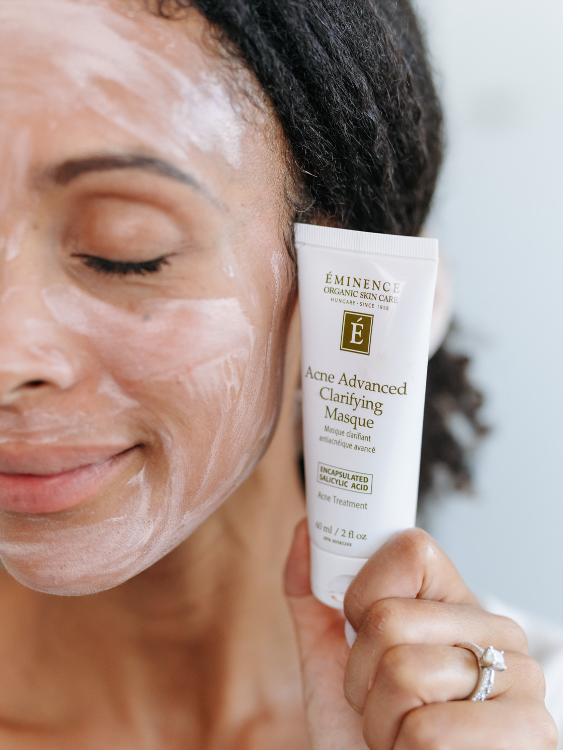 A woman holding Eminence Organics Acne Advanced Clarifying Masque 