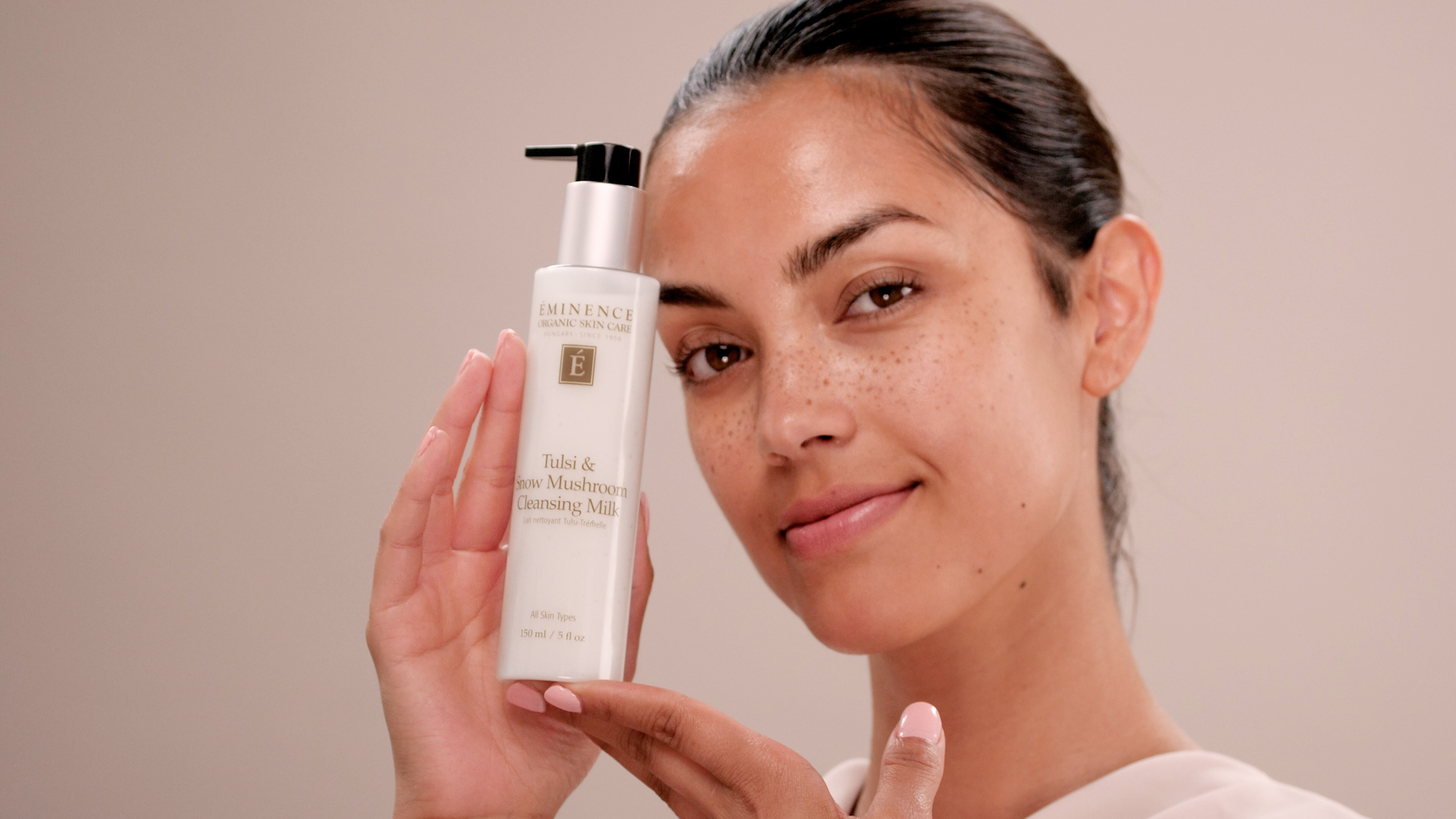 A woman holding Eminence Organics Tulsi & Snow Mushroom Cleansing Milk