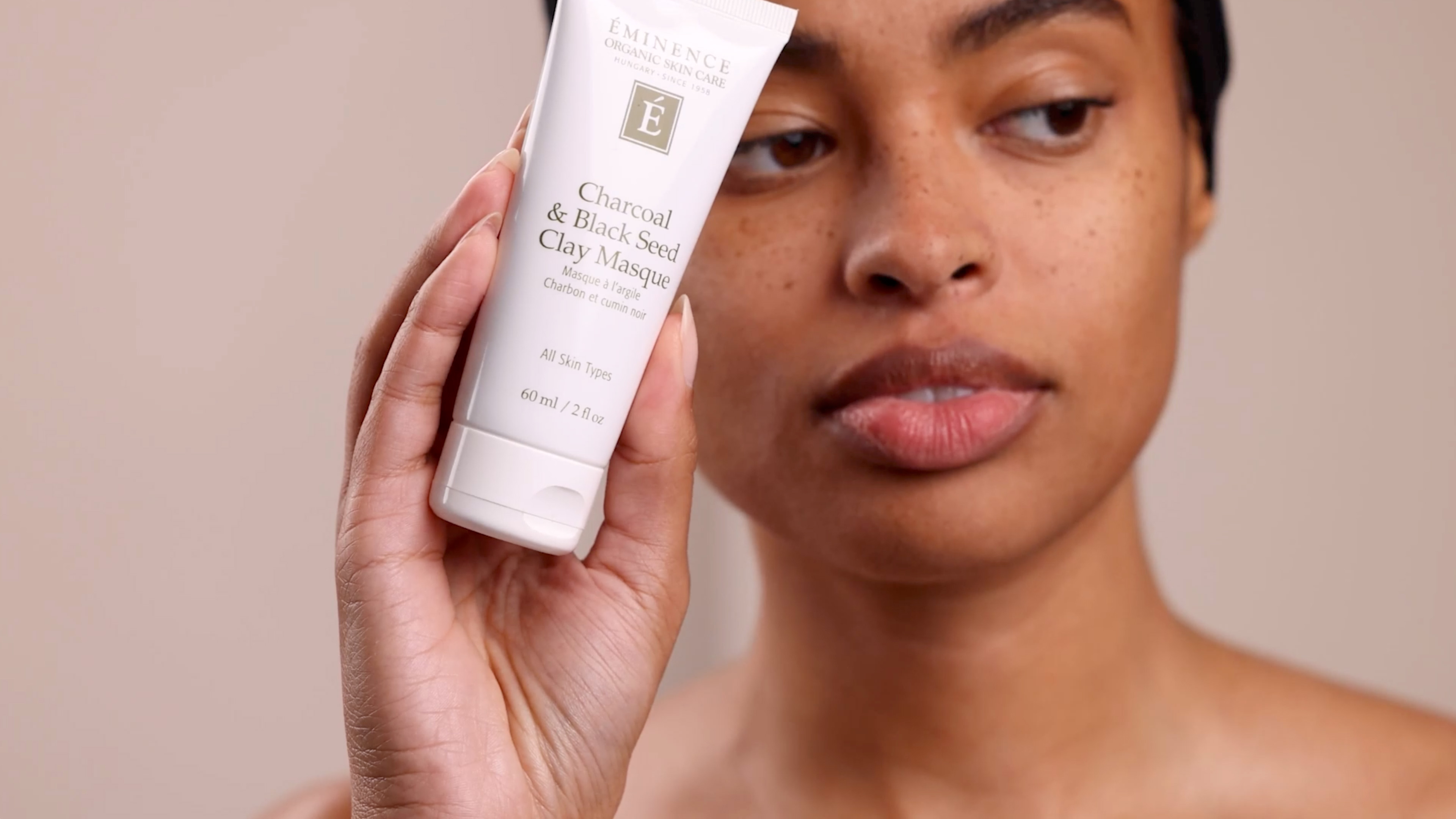 A woman holding Eminence Organics Charcoal & Black Seed Clay Masque
