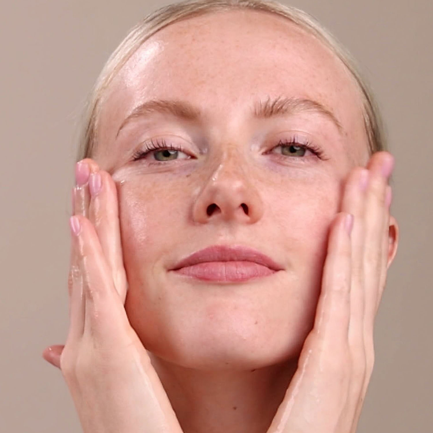 A woman washing her face with the Eminence Organics Firm Skin Acai Cleanser
