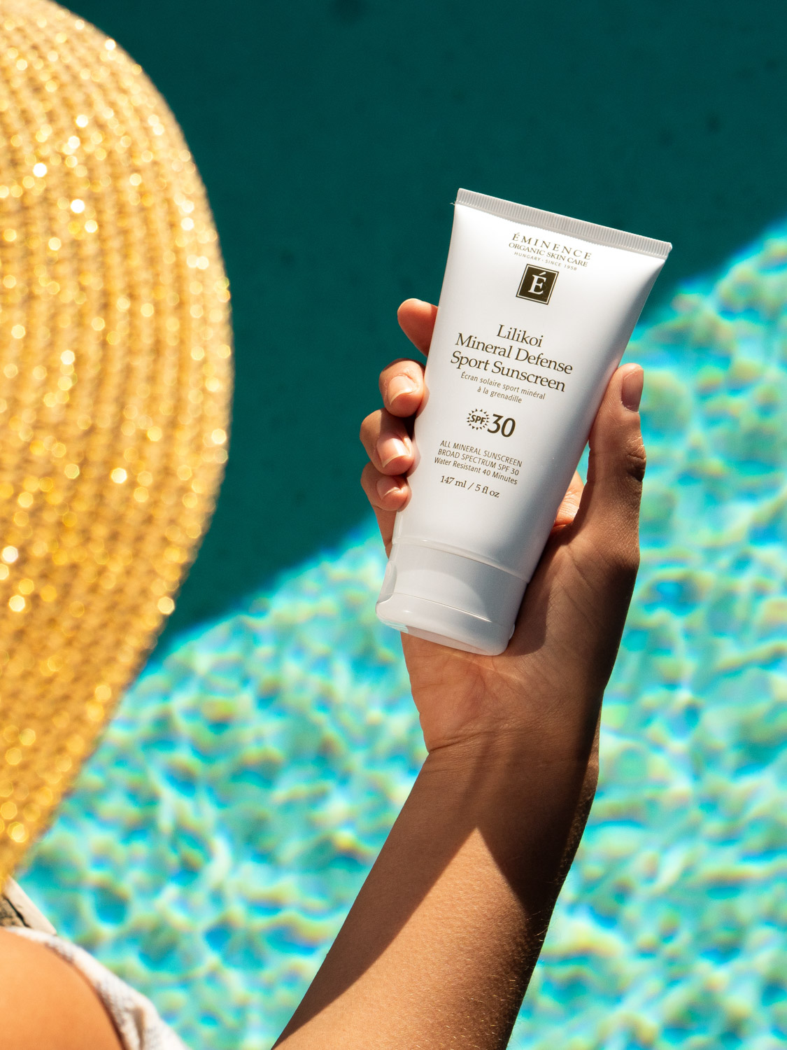 A woman holding the Eminence Organics Lilikoi Mineral Defense Sport Sunscreen SPF 30 tube by a pool