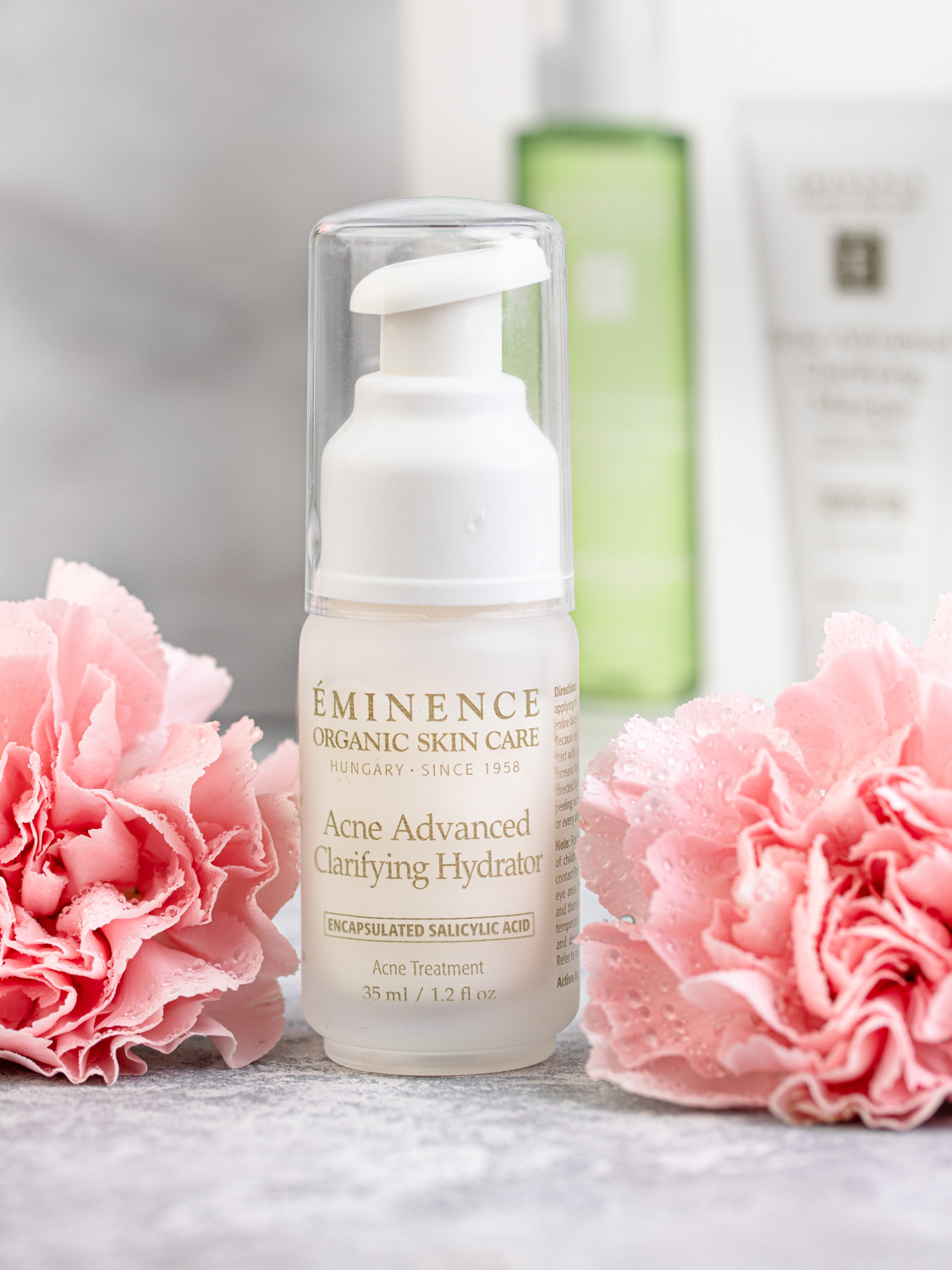Eminence Organics Acne Advanced Clarifying Hydrator surrounded by pink flowers