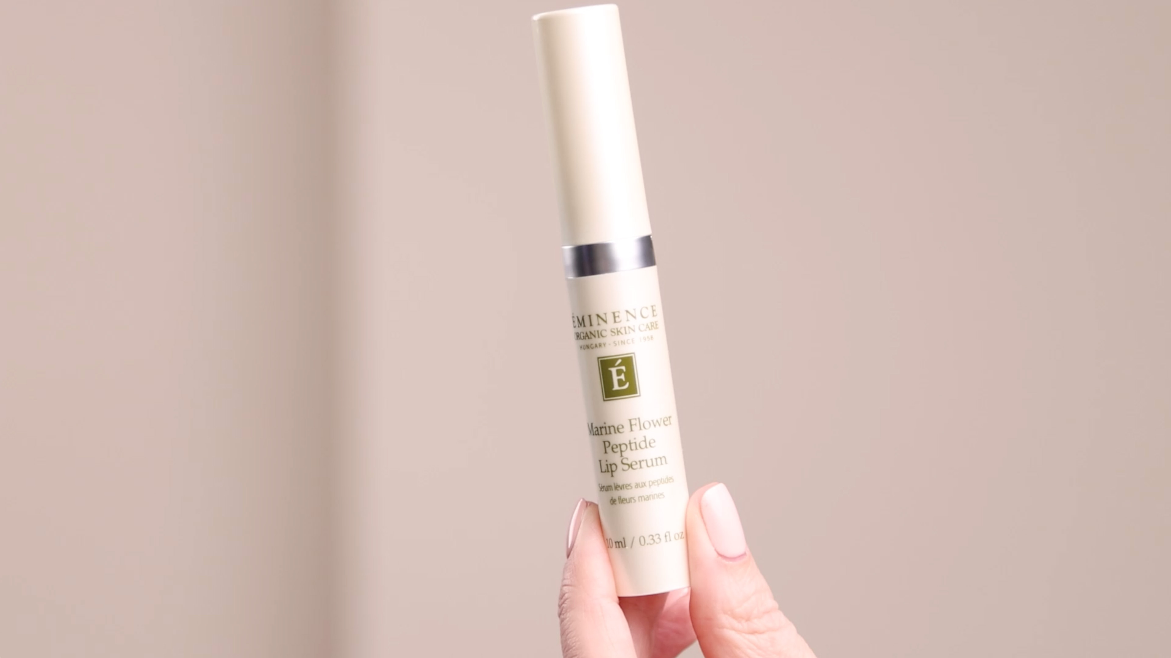 A hand holding the Eminence Organics Marine Flower Peptide Lip Serum tube