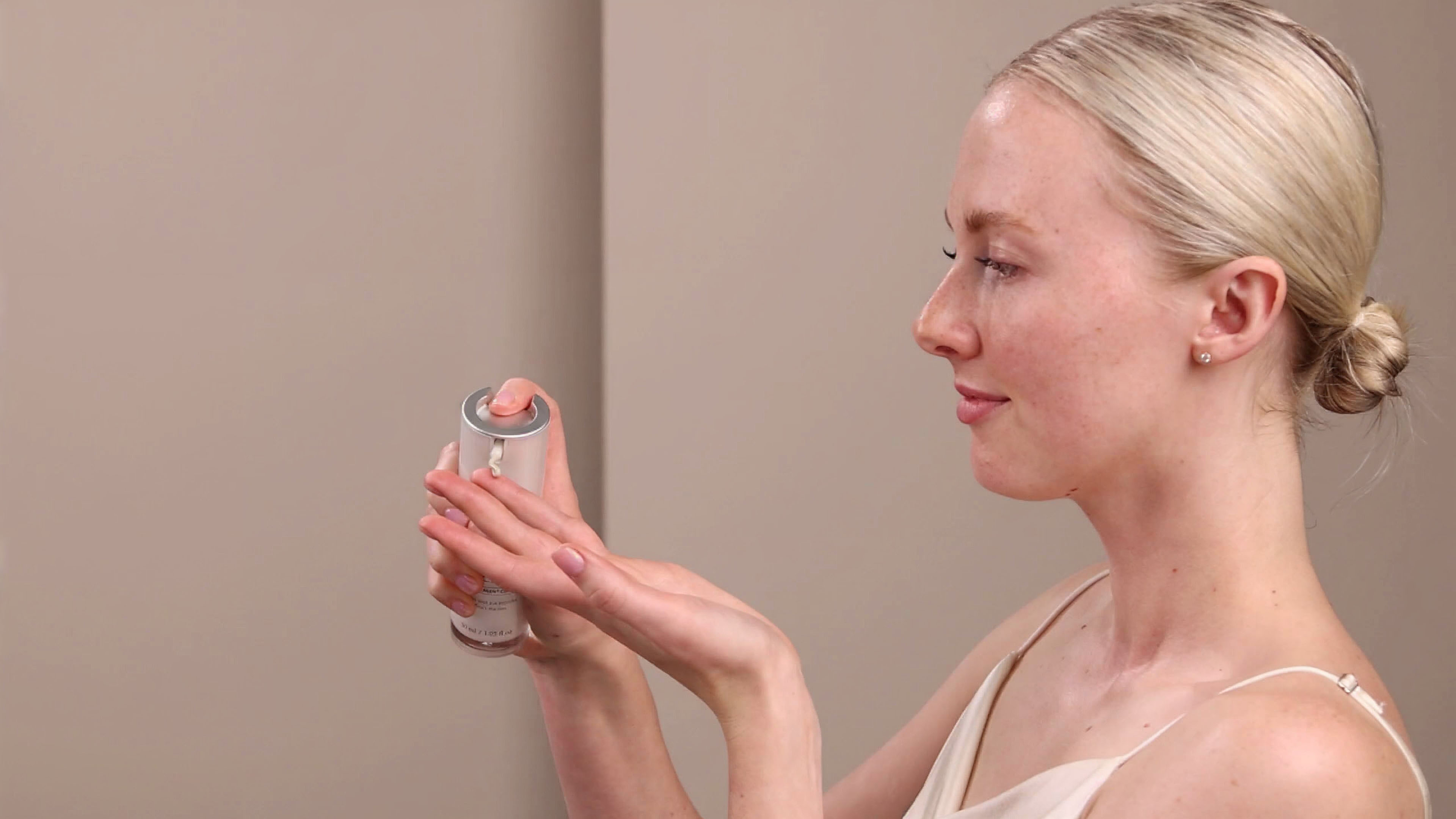 A woman holding the Eminence Organics Marine Flower Peptide Eye Cream Bottle next to their face