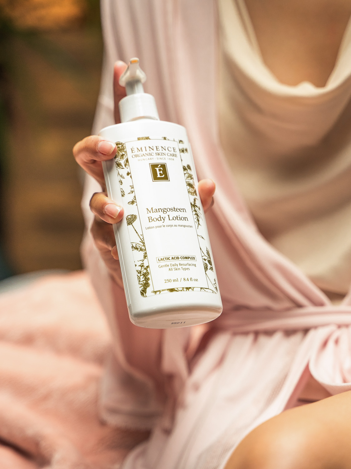 A woman holding the Eminence Organics Mangosteen Body Lotion bottle