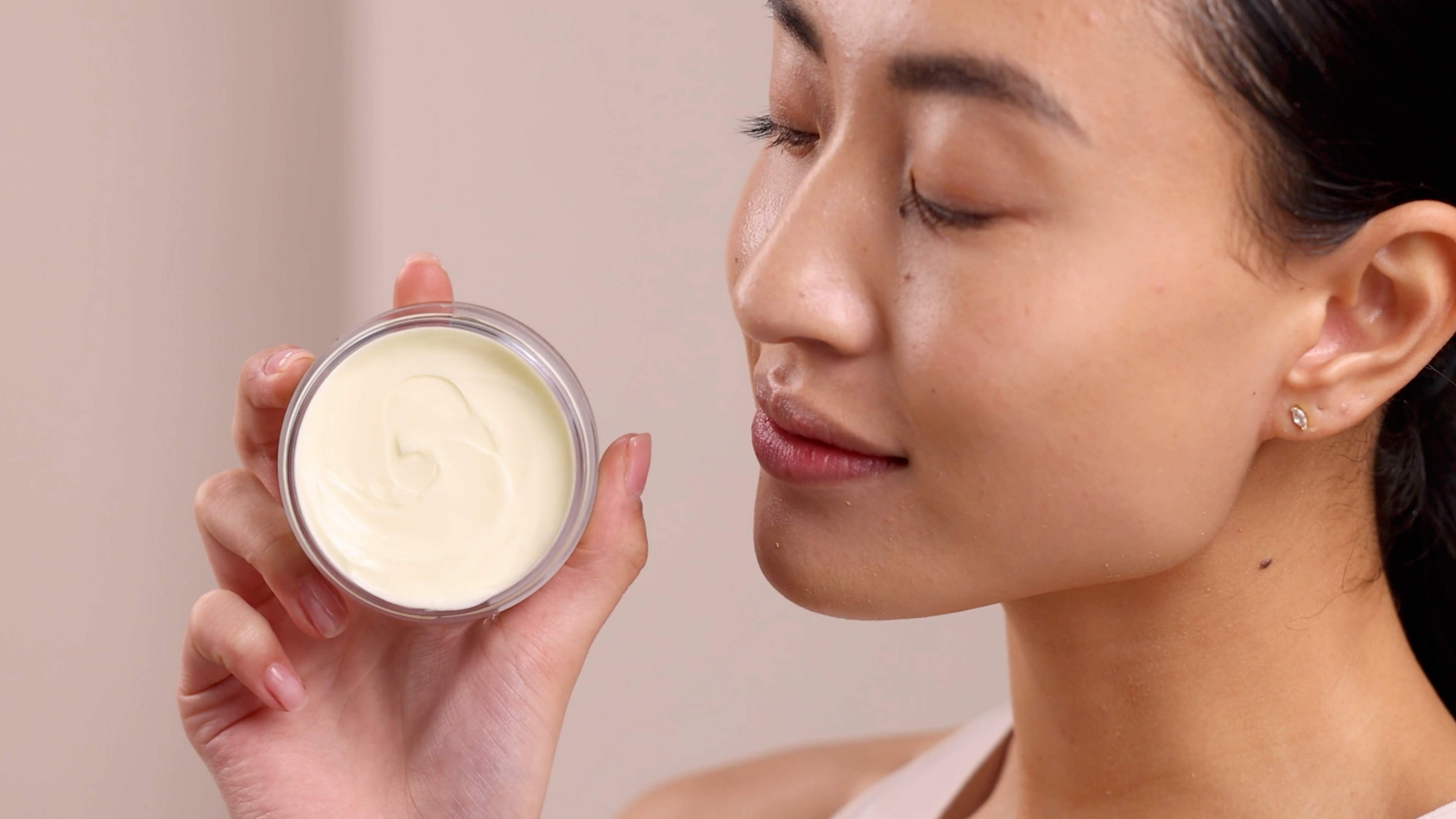 A woman holding the Eminence Organics Monoi Age Corrective Night Cream for Face & Neck Jar next to her face