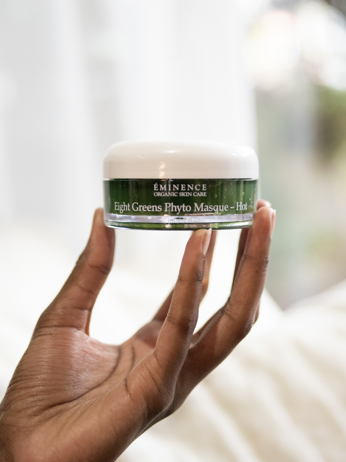A hand holding the Eminence Organics Eight Greens Phyto Masque – Hot jar